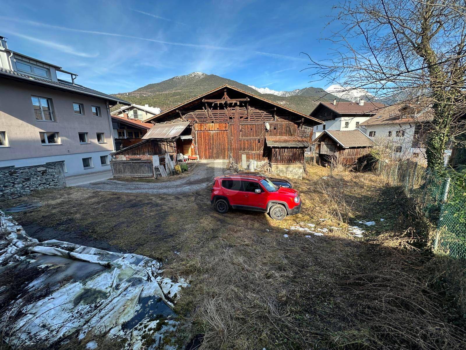 Großes Holzgebäude mit einem roten Auto auf einem Grundstück vor einer Bergkulisse.