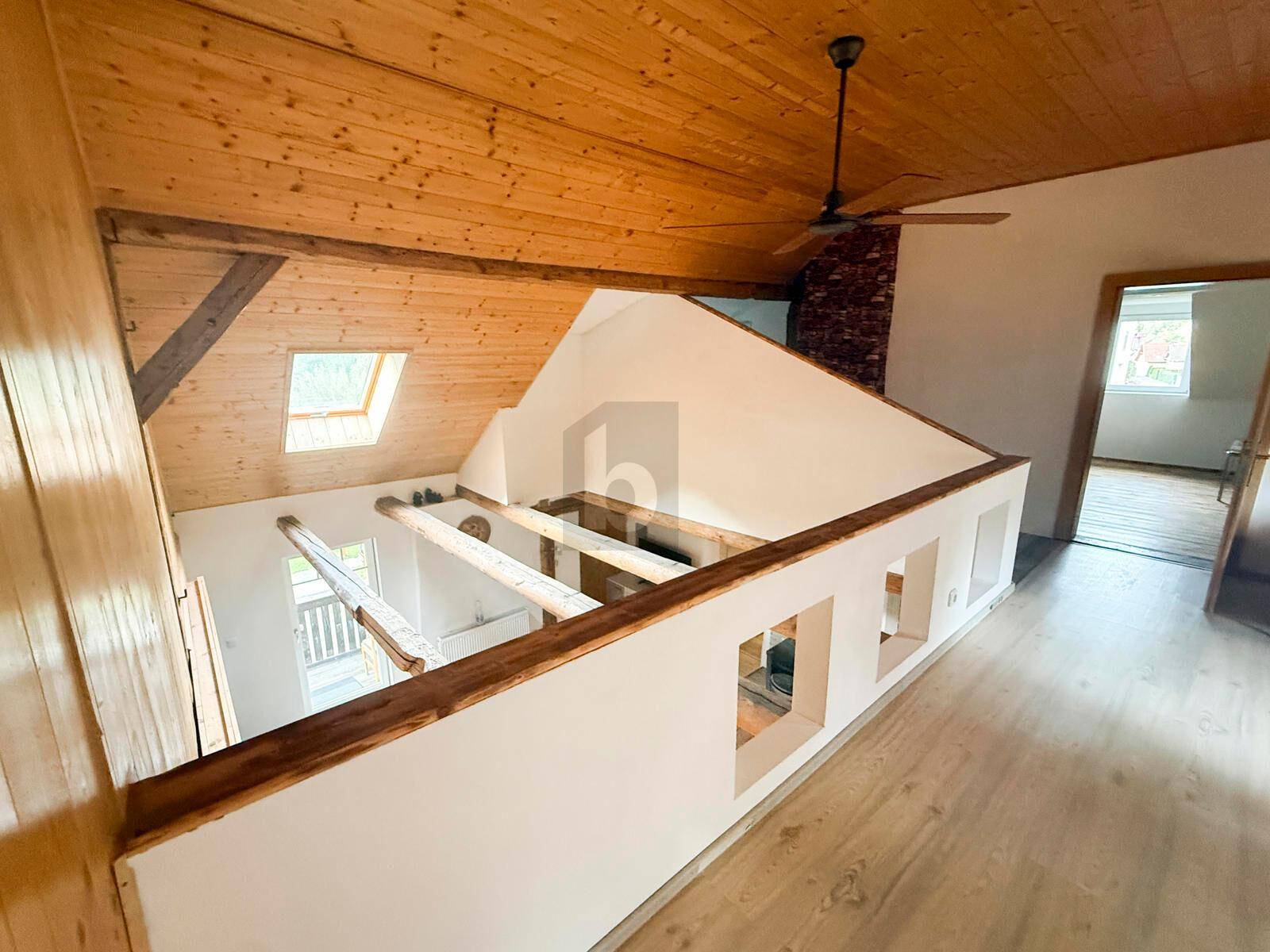 Galeriebereich mit Blick nach unten, Holzbalken, Holzdecke, Deckenventilator und Dachfenstern.