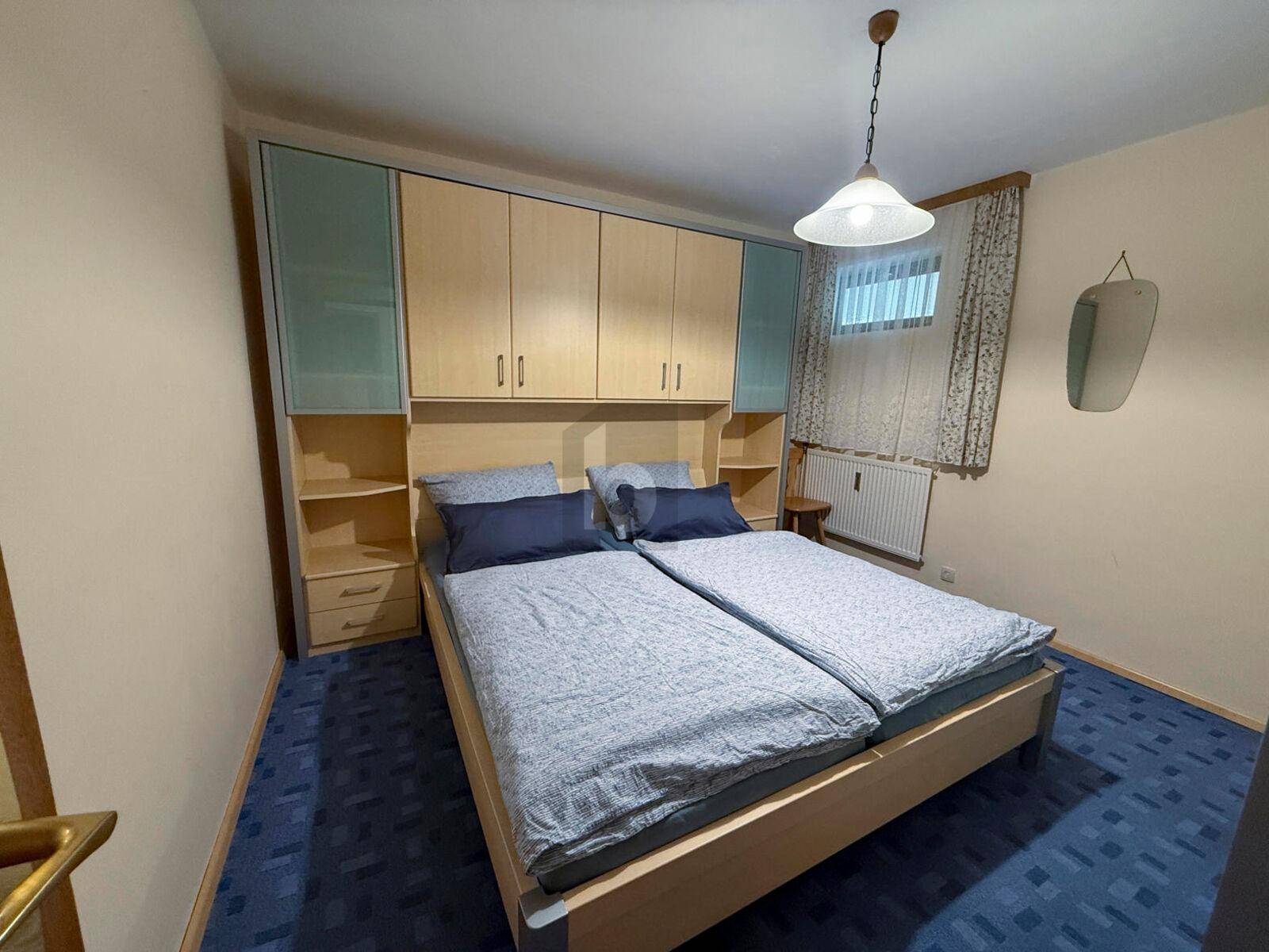 Schlafzimmer mit Doppelbett, Einbauschränken und blauem Teppichboden.