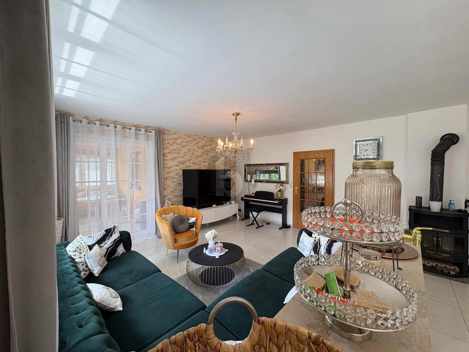 Gemütliches Wohnzimmer mit großem grünen Sofa, Kaminofen und Klavier.