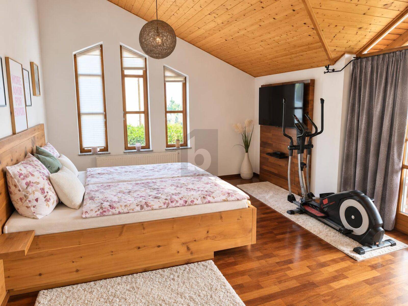 Helles Schlafzimmer mit Holzboden, schrägen Decken und großen Fenstern sowie einem Fitnessgerät.