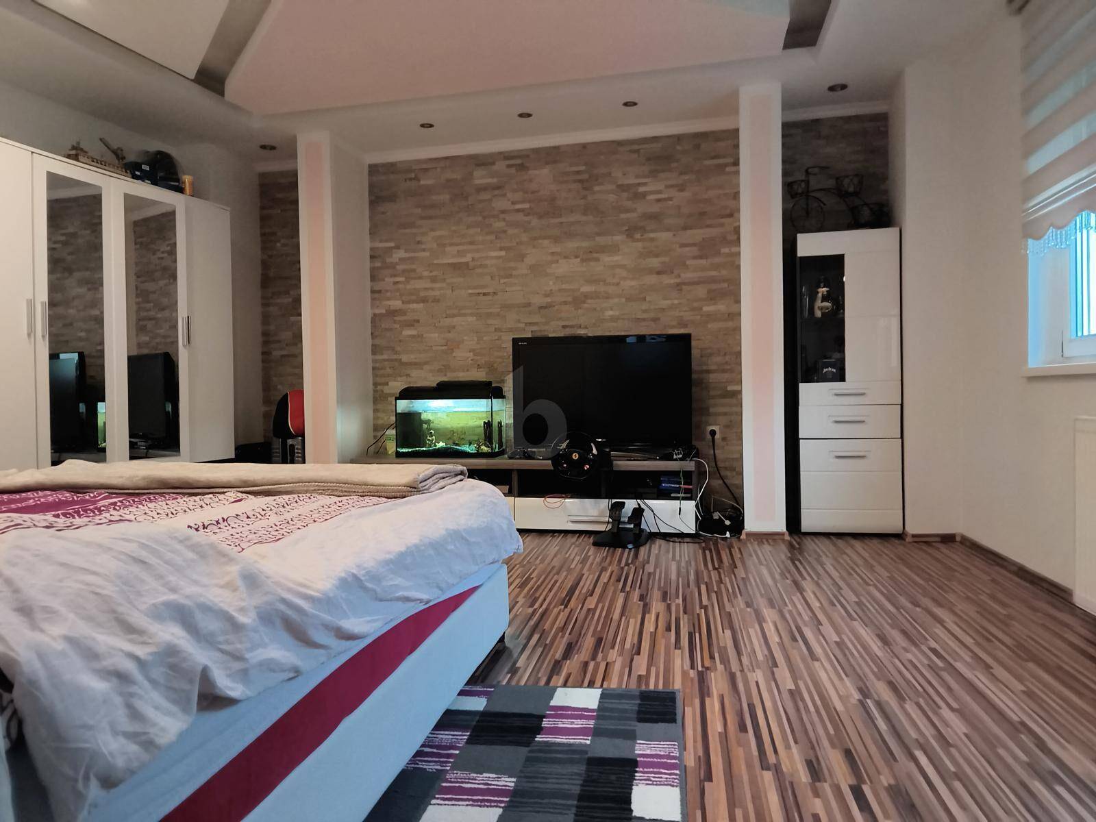Geräumiges Schlafzimmer mit Holzboden, einer strukturierten Wand und großem Bett.