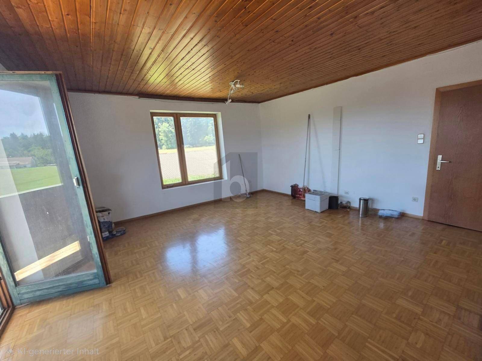 Leeres Zimmer mit Parkettboden, Holzdecke und Zugang zu einem Balkon mit Blick ins Grüne.