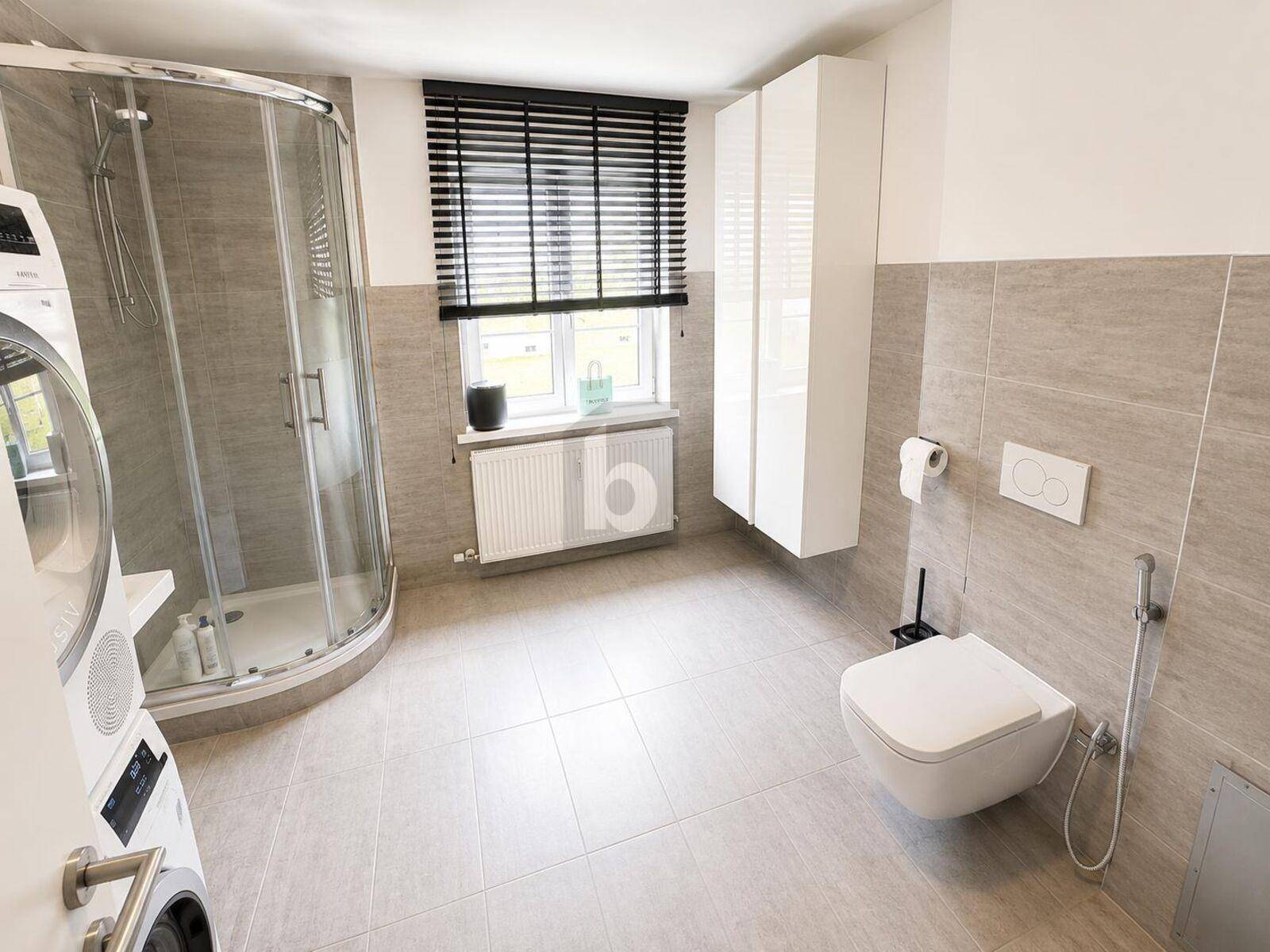 Modernes Badezimmer mit Duschkabine, wandhängendem WC und Waschmaschine.