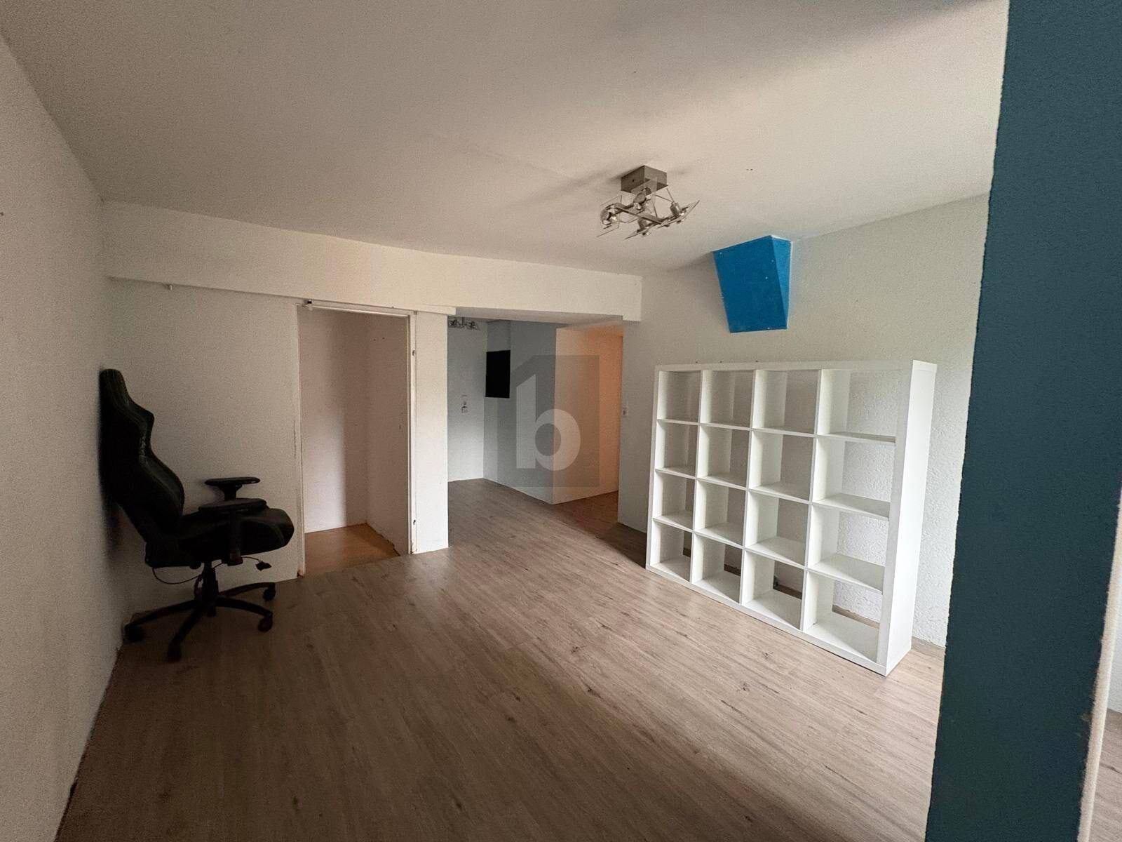 Vielseitiger Raum mit Holzboden und großem Regal, ideal als Büro oder Gästezimmer.