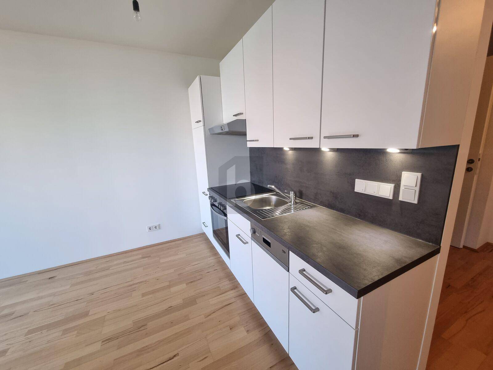 Moderne Küchenzeile mit weißen Schränken, dunkler Arbeitsplatte und integrierten Geräten.