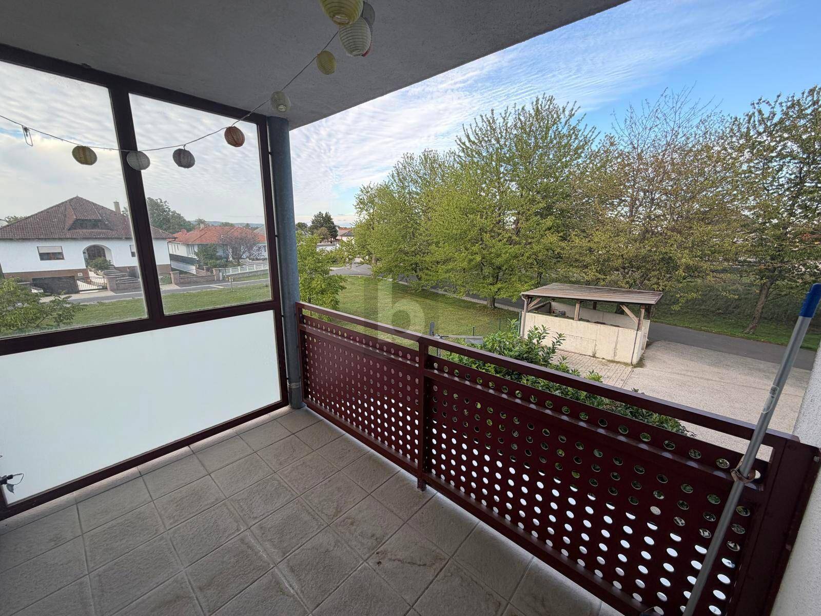 Balkon mit Fliesenboden und Blick ins Grüne sowie auf umliegende Häuser.