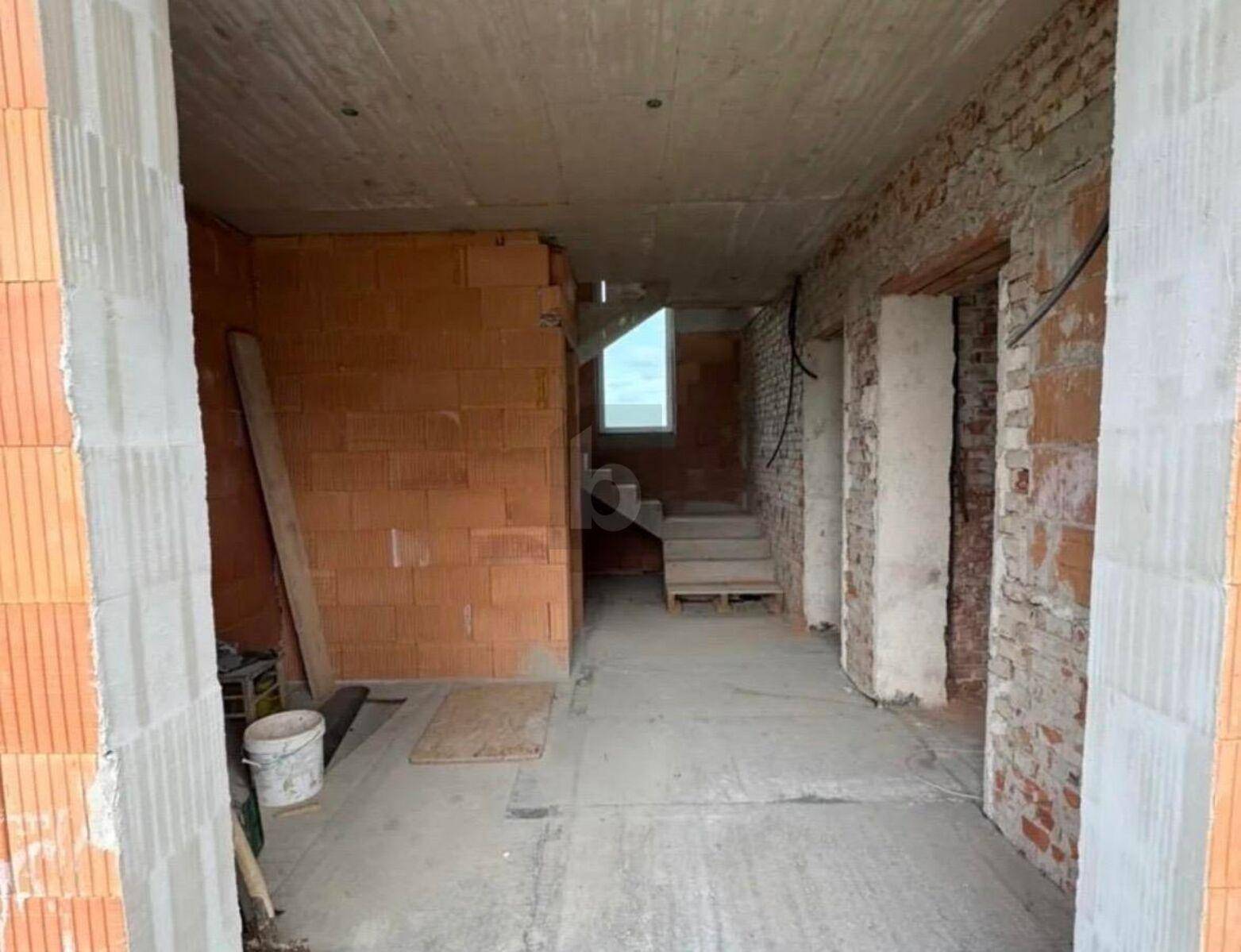 Unfertiger Innenraum im Rohbau mit sichtbaren Ziegelwänden und Betontreppe, bereit für den Ausbau.