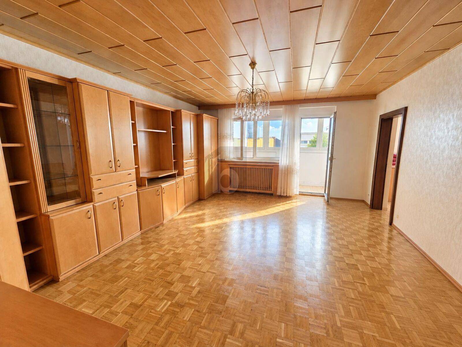 Großzügiges Wohnzimmer mit Parkettboden, Holzdecke und Zugang zu einem kleinen Balkon.