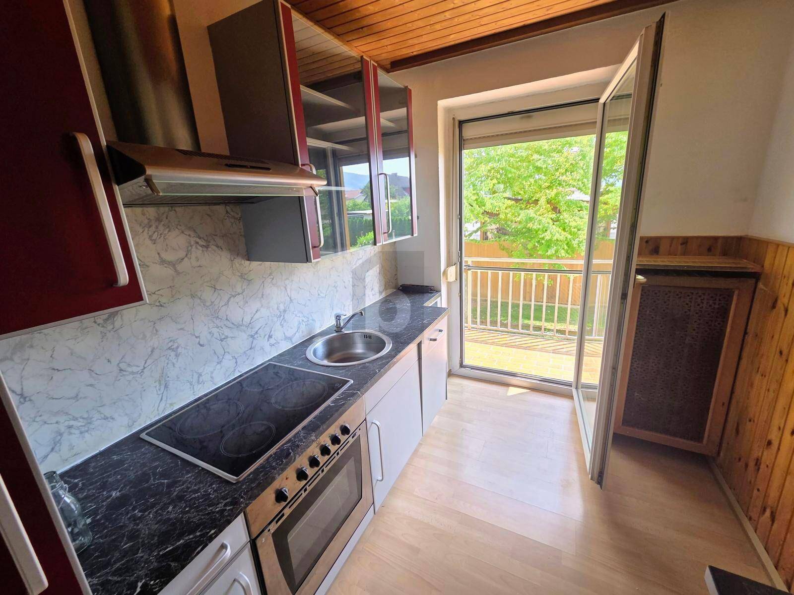 Kleine Küche mit Einbaugeräten, Holzdecke und Zugang zu einem Balkon.