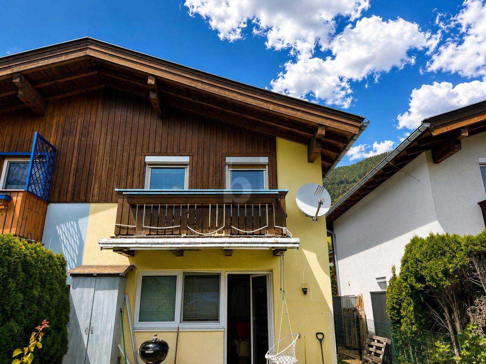 Gelbe Hausfassade mit traditionellem Holzbalkon und einem Grillbereich im Erdgeschoss.