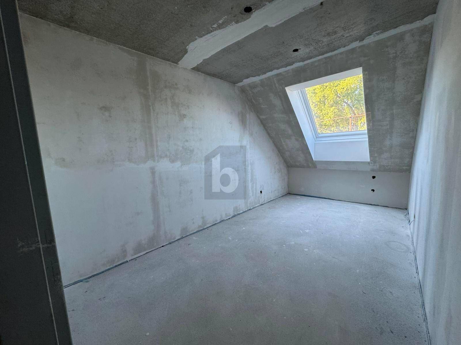 Unfertiger Raum im Dachgeschoss mit schräger Decke und einem großen Dachfenster.