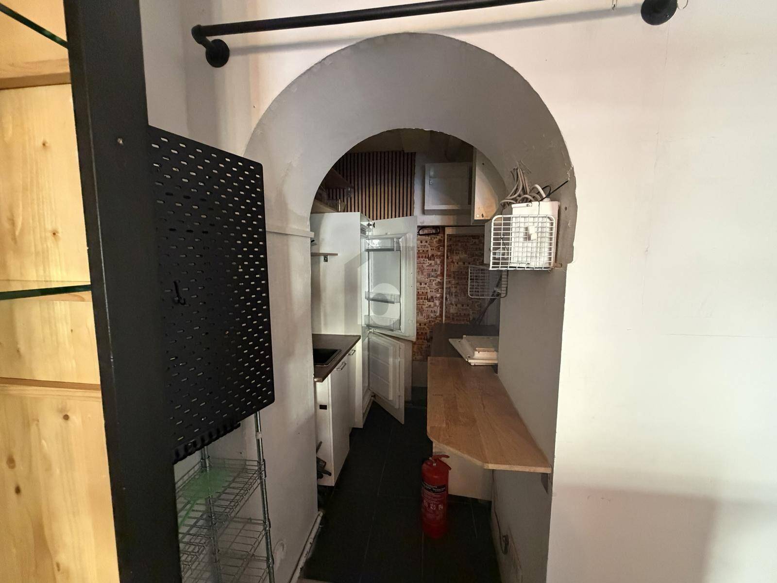Kleine Küchenzeile oder Lagerbereich mit Kühlschrank und Arbeitsplatte unter einem Gewölbebogen.