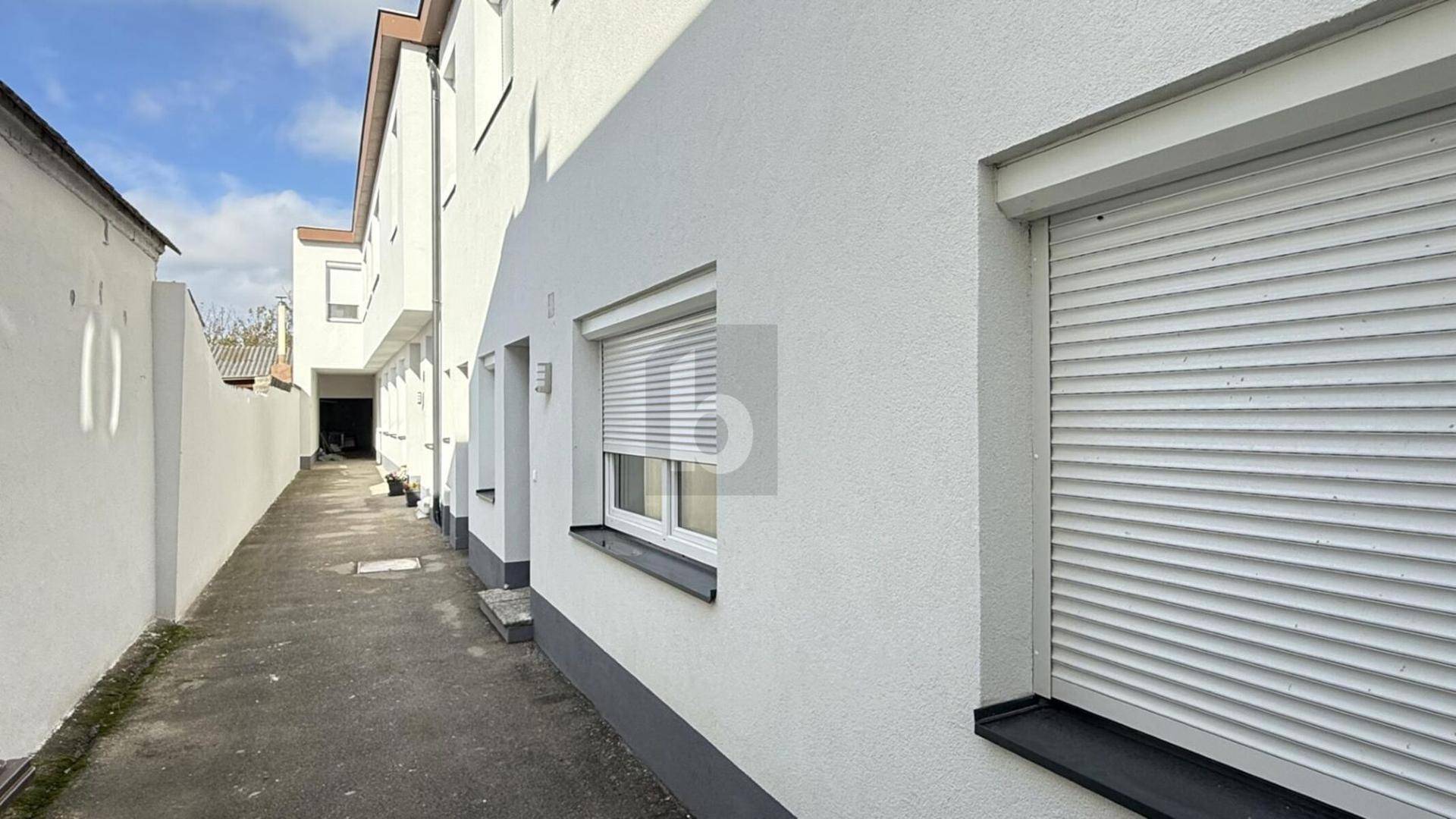 Seitenansicht des Gebäudes mit weißer Fassade und einem schmalen Durchgang zum Hinterhof.