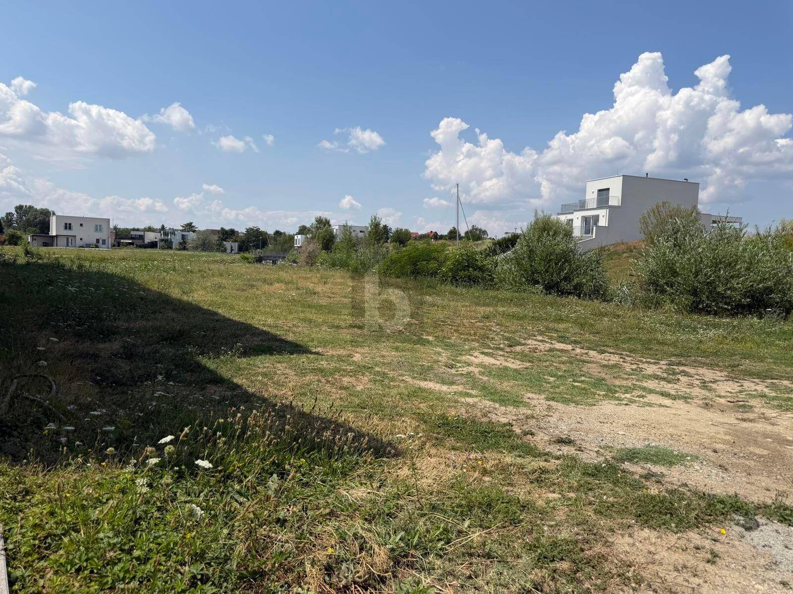 Großes, sonniges Grundstück mit Grasfläche und modernen Häusern in der Ferne.