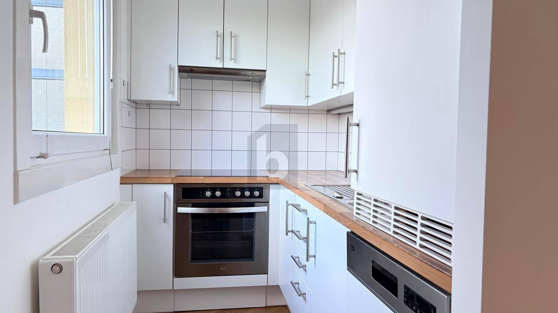 Kompakte Einbauküche mit weißen Schränken, Holz-Arbeitsplatte und modernen Geräten.