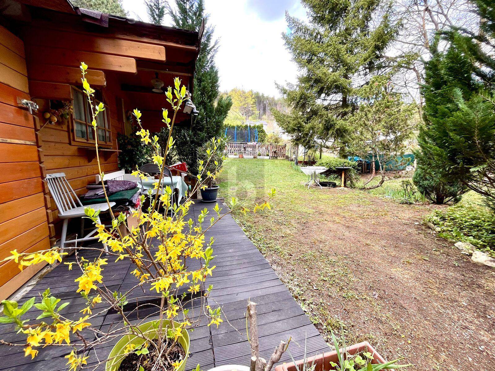Hölzerne Terrasse neben dem Gartenhaus mit Topfpflanzen und Blick auf den weitläufigen Garten.