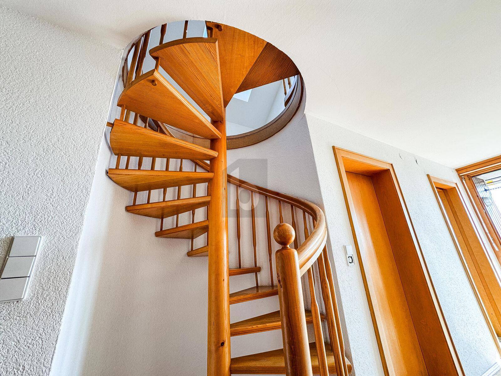 Elegante Holz-Wendeltreppe in einem hellen Treppenhaus, die verschiedene Ebenen verbindet.