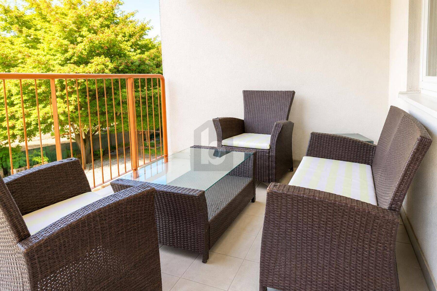 Gemütlicher Balkon mit Rattanmöbeln und einem Glastisch, umgeben von viel Grün.