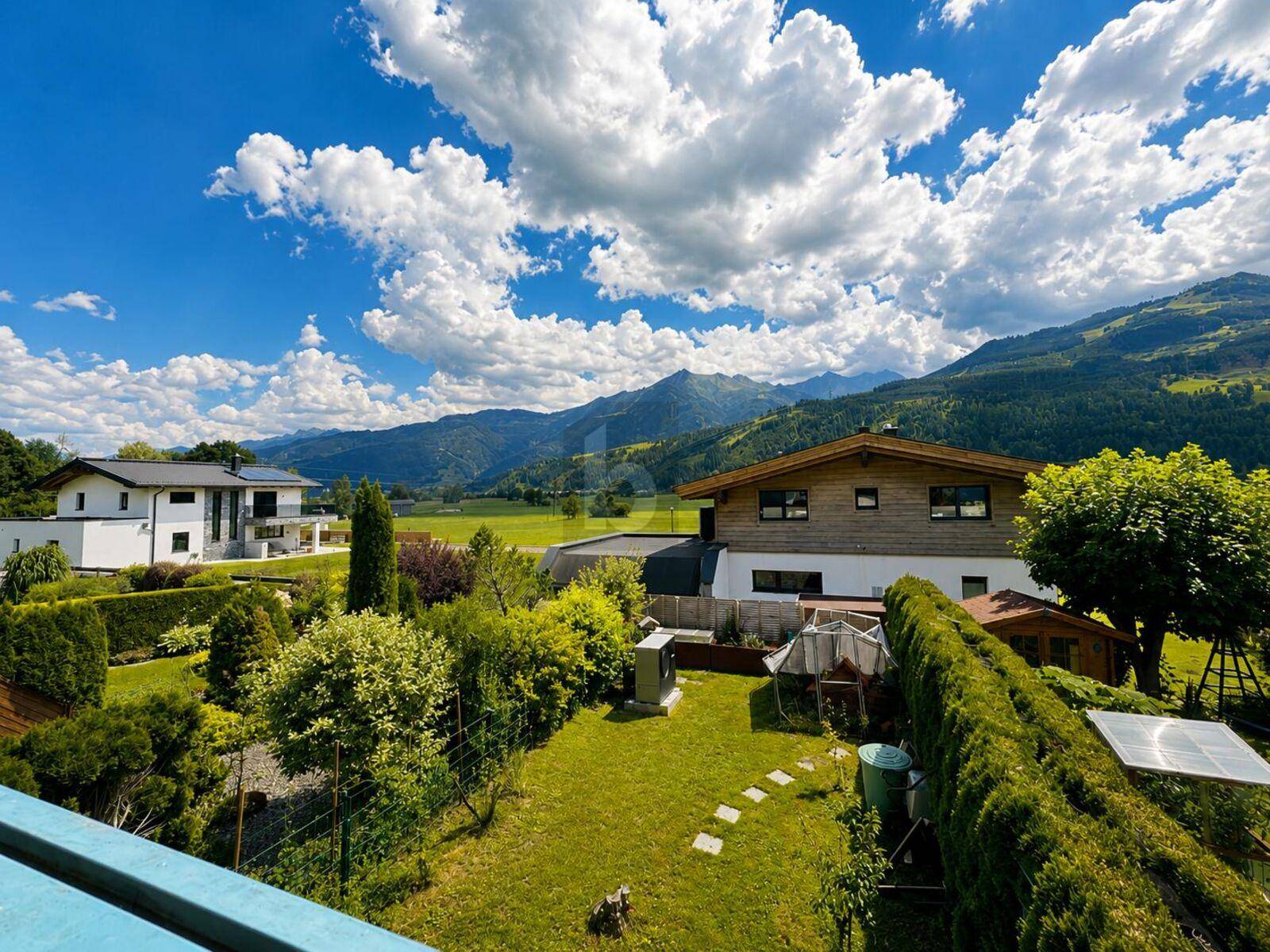 Weitläufiger Garten mit Rasen und Hecken, umgeben von einer malerischen Bergkulisse und weiteren Häusern.