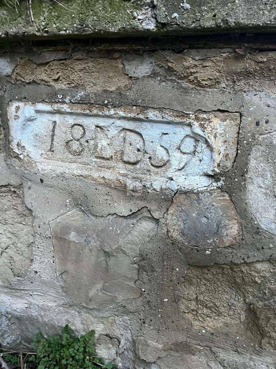 Nahaufnahme einer alten Steinmauer mit einer eingemeißelten Jahreszahl '18D59'.