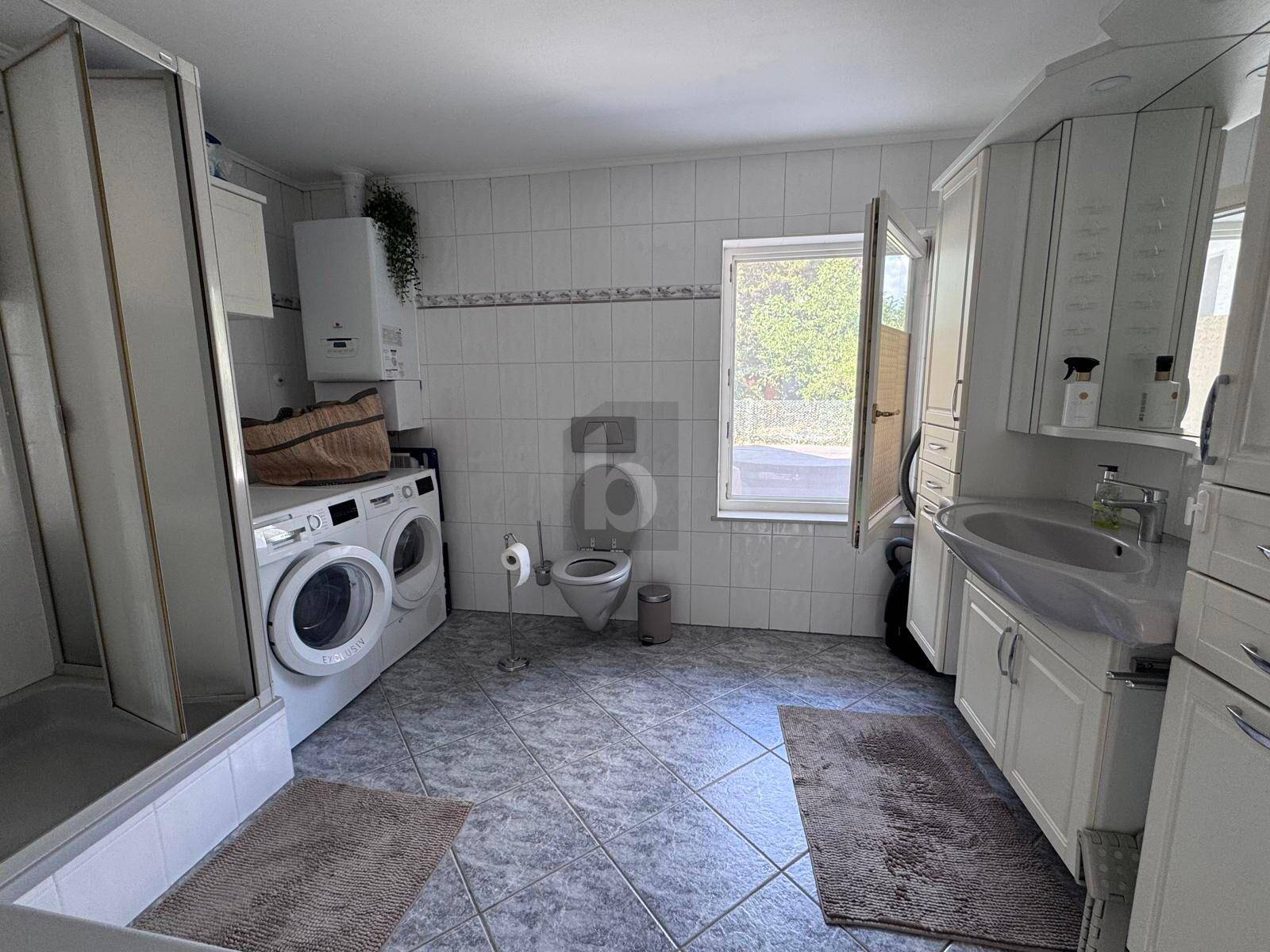 Helles Badezimmer mit Fliesenboden, Dusche, Waschbecken und integriertem Spiegelschrank.