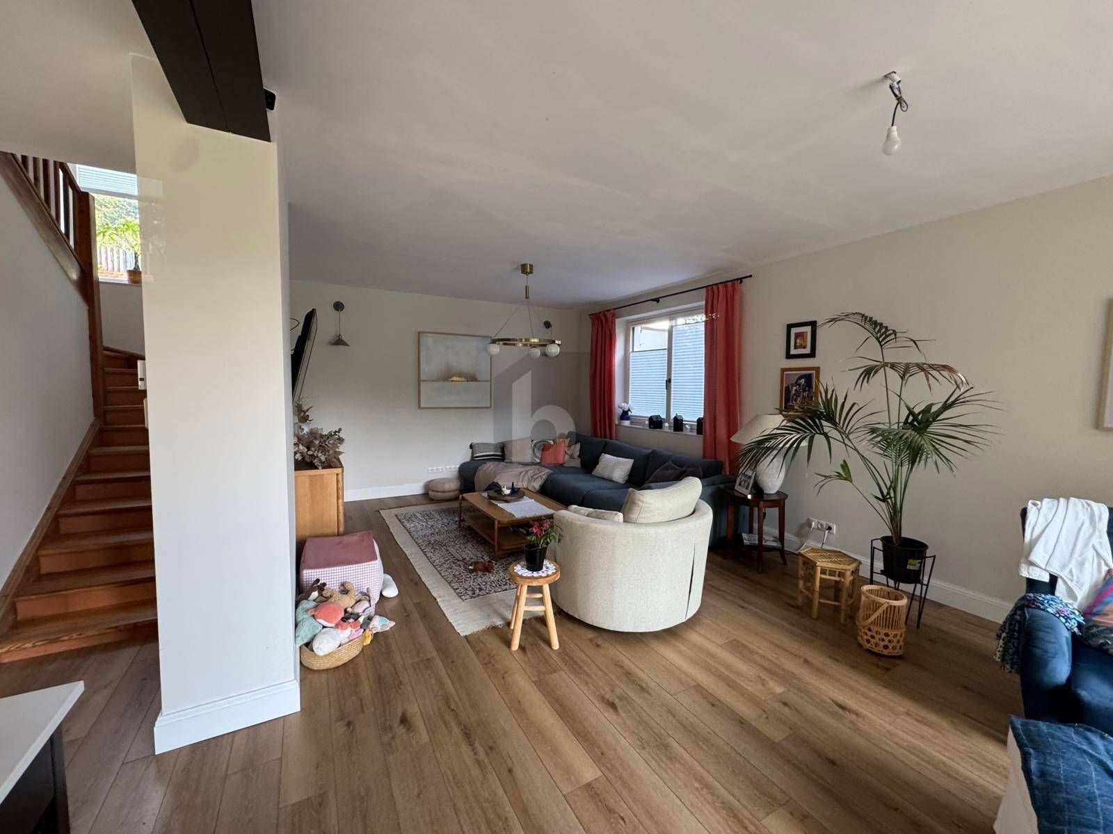 Gemütliches Wohnzimmer mit Holzboden, bequemen Möbeln und Zugang zu einer Holztreppe.