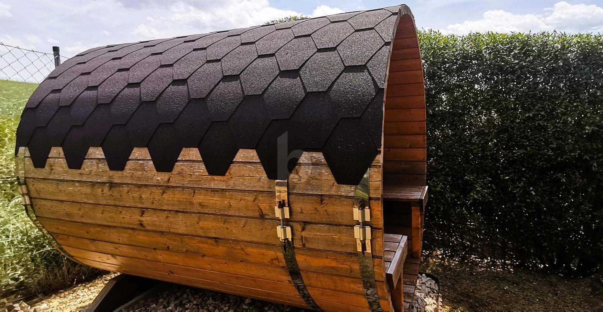 Fasssauna im Gartenbereich mit dunklem Schindeldach und Holzbänken.