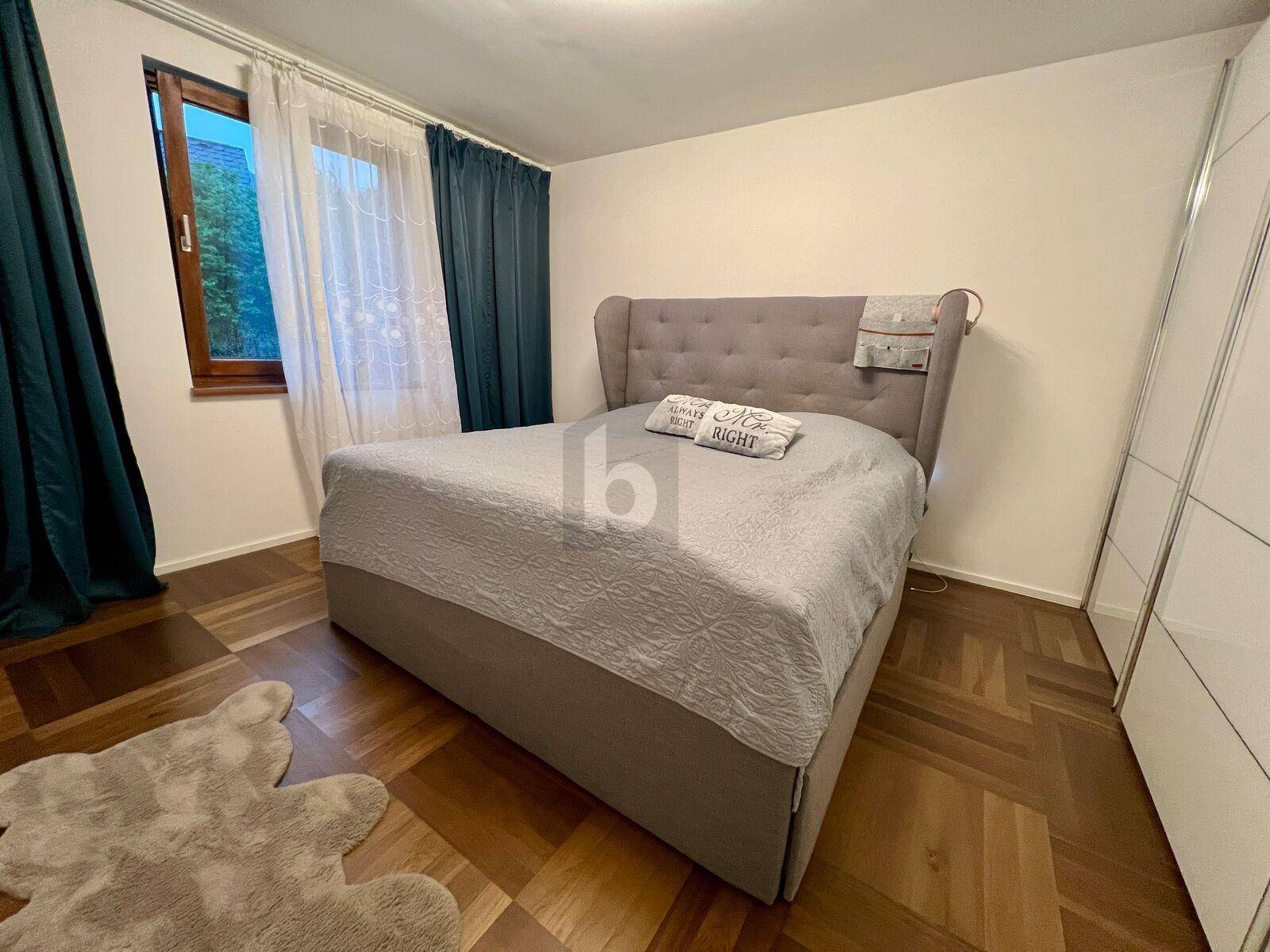 Schlafzimmer mit bequemem Polsterbett, dunklen Vorhängen und elegantem Parkettboden.