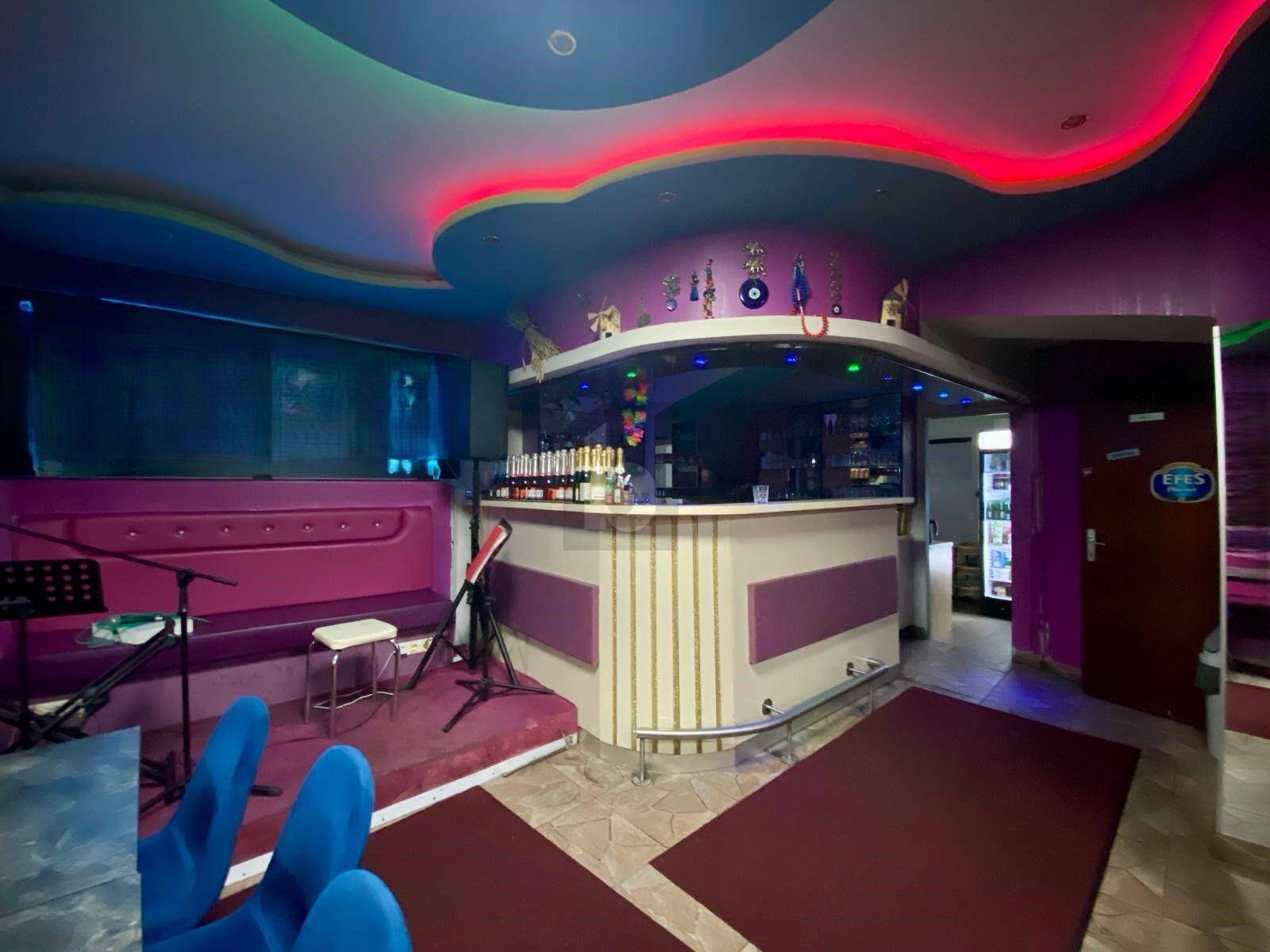 Die Bar des Lokals mit einer Theke, Flaschenregalen und einem kleinen Bühnenbereich für Unterhaltung.