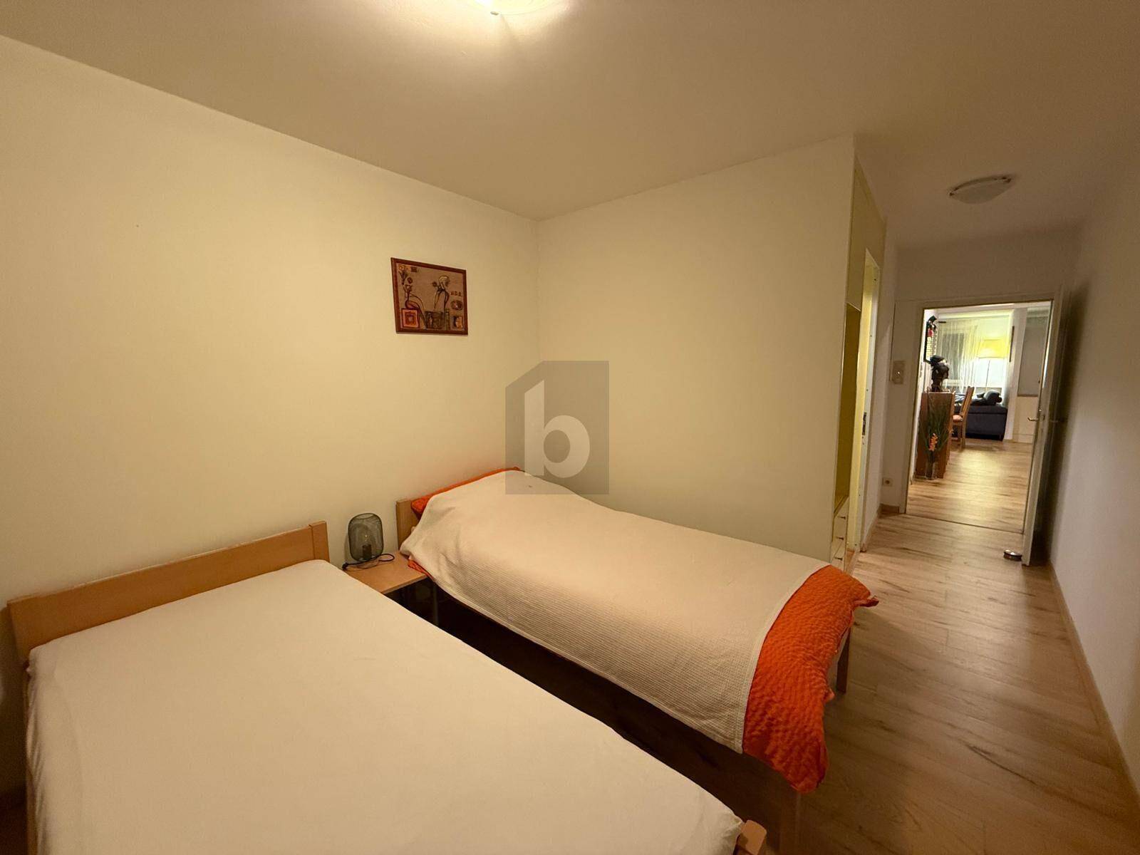 Schlafzimmer mit zwei Einzelbetten, einem Nachttisch und Blick in den angrenzenden Flurbereich.