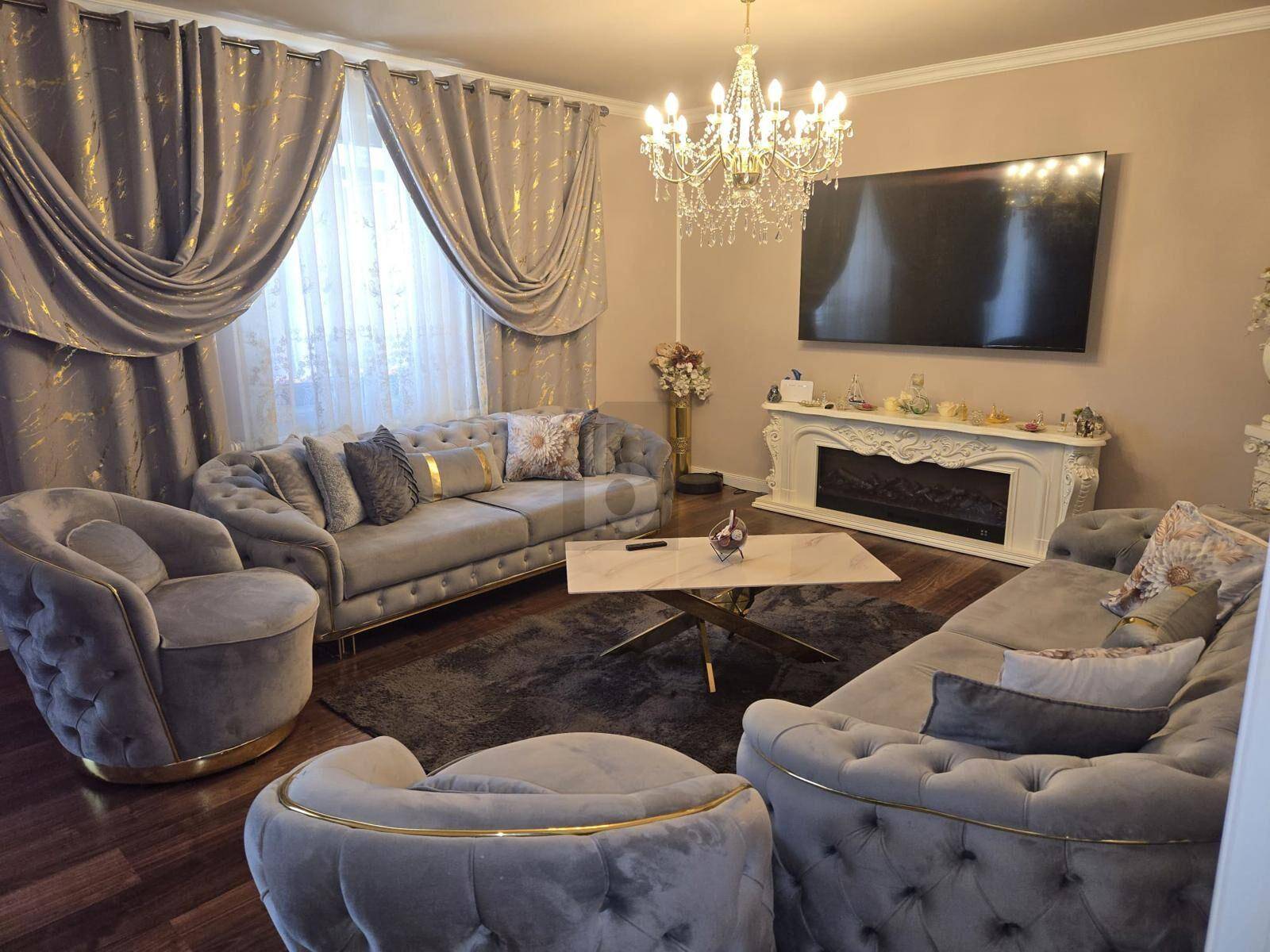 Elegantes Wohnzimmer mit grauen Samtsofas, Marmortisch, großem Fernseher und einem dekorativen Kamin.