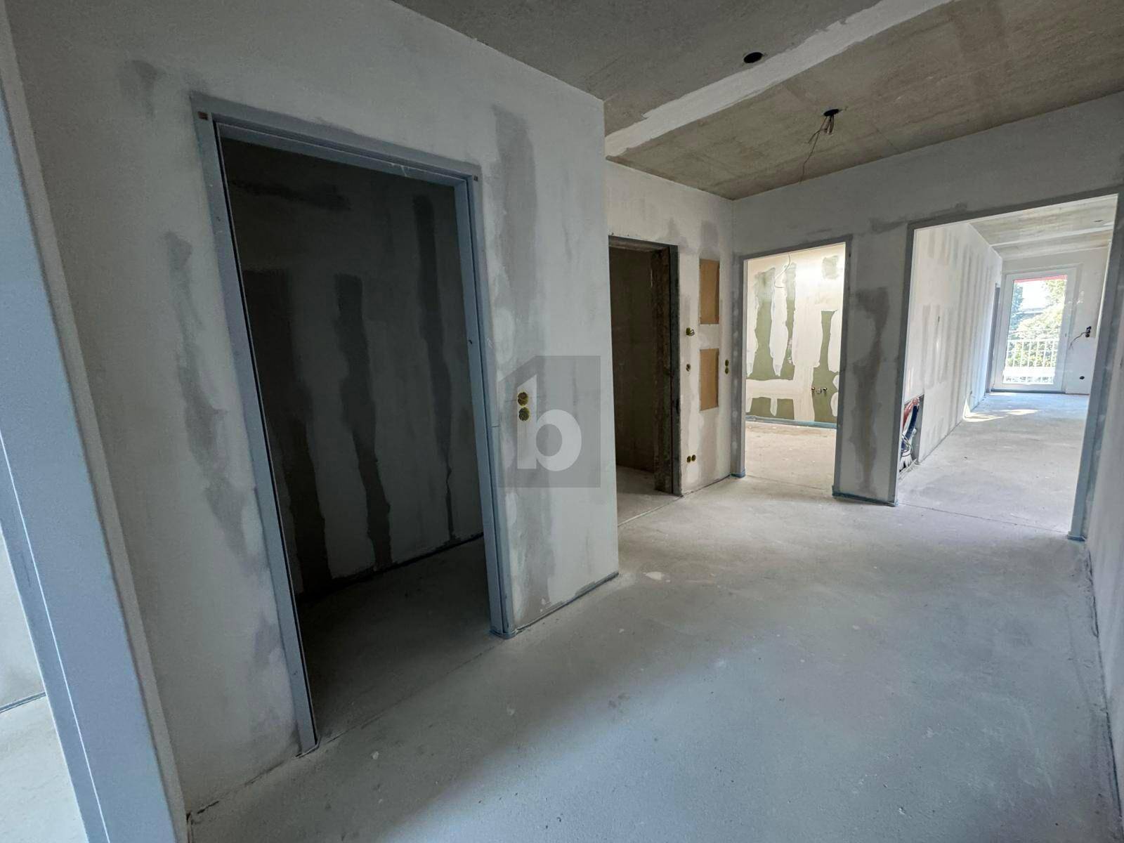 Unfertiger Flur mit mehreren Türöffnungen zu weiteren Räumen und Betonboden.