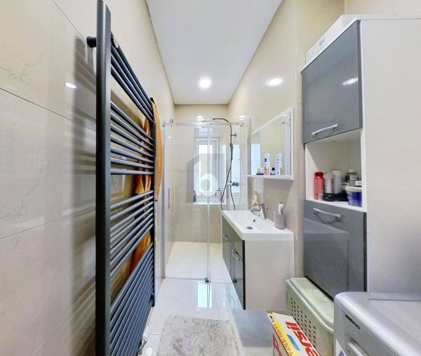 Schmales, modernes Badezimmer mit begehbarer Dusche, beheiztem Handtuchhalter und hellen Fliesen.