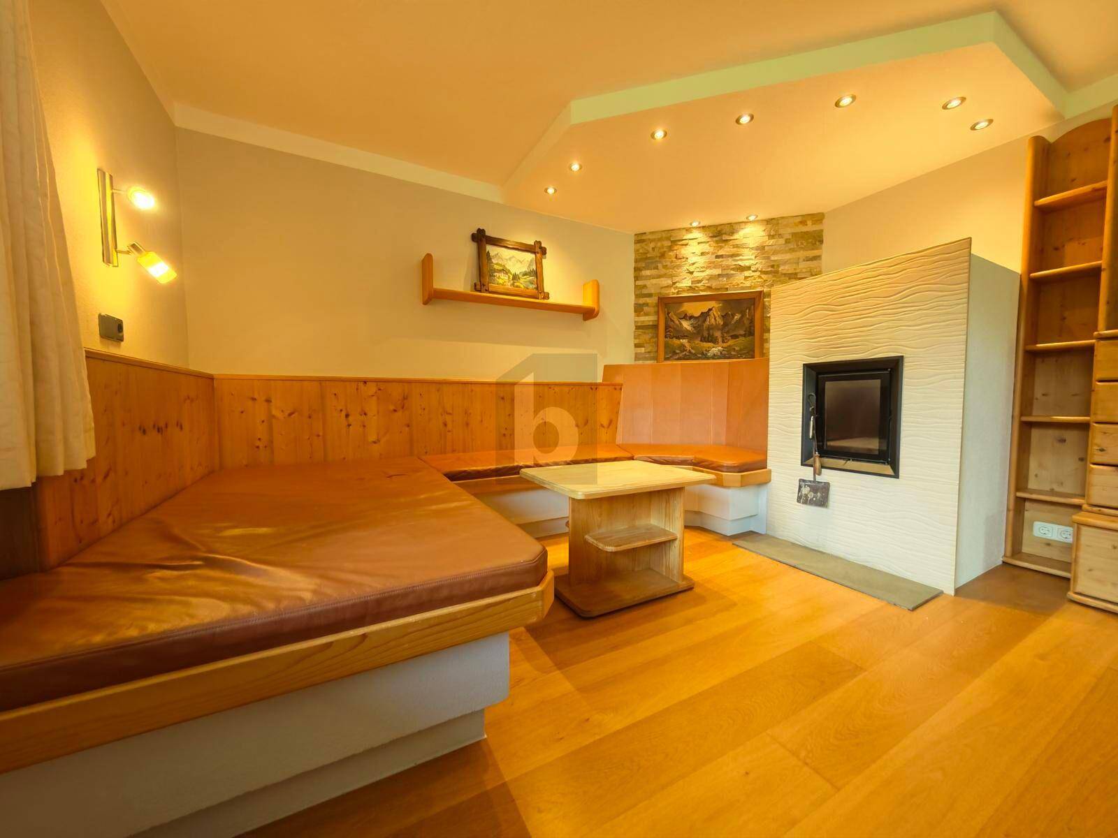 Gemütliches Wohnzimmer im alpinen Stil mit Holzbänken, Holzboden und einem Kachelofen.