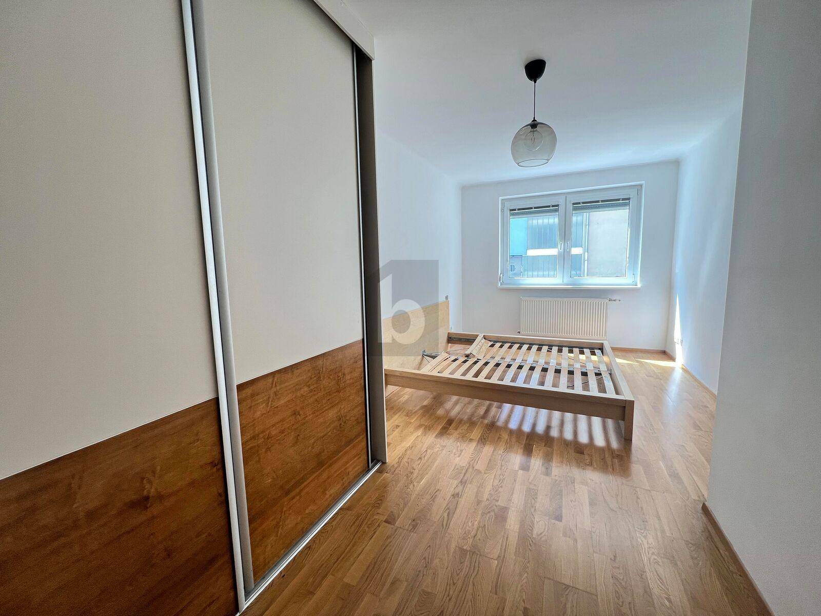 Helles Schlafzimmer mit Parkettboden, Fenster und großem Schiebetürenschrank.