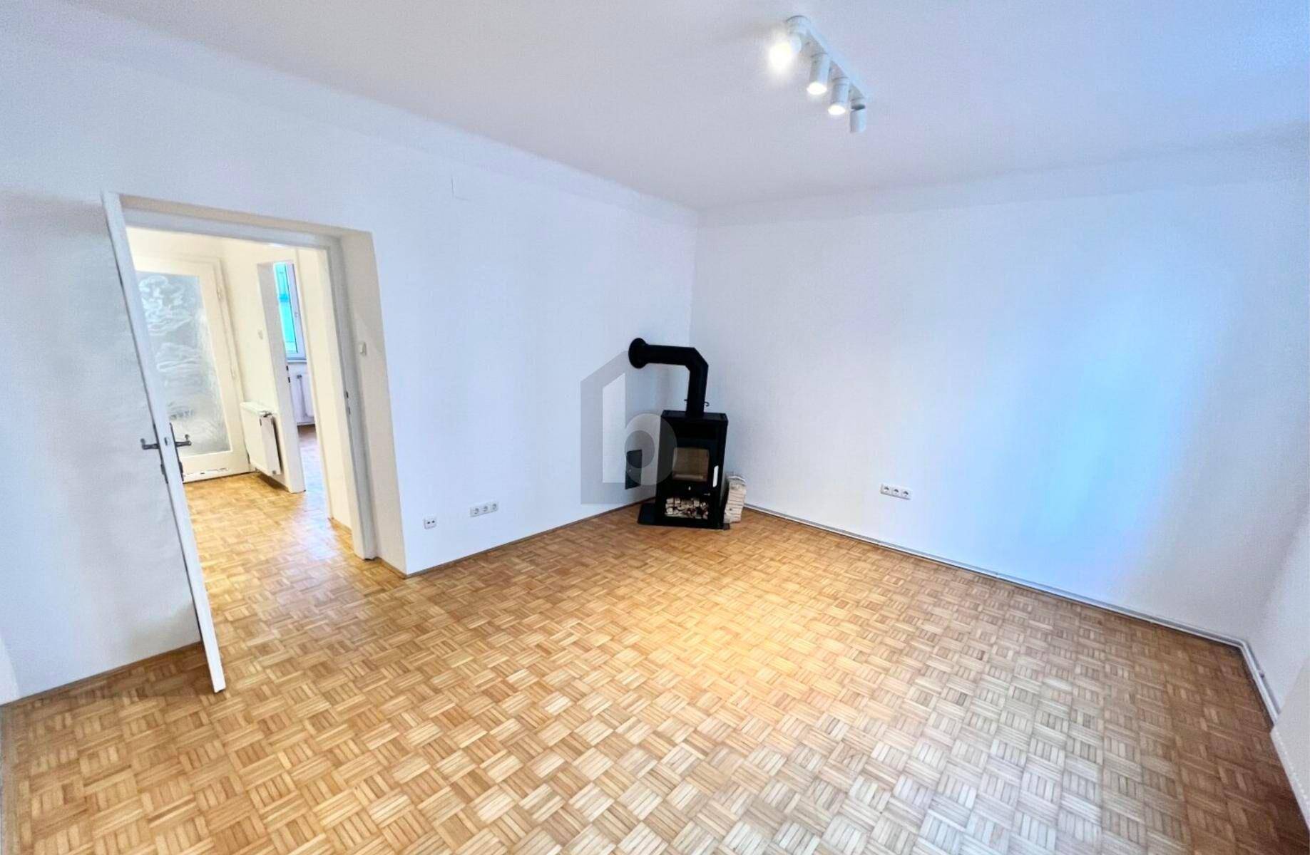Geräumiges Wohnzimmer mit Parkettboden und einem gemütlichen Holzofen als Wärmequelle.