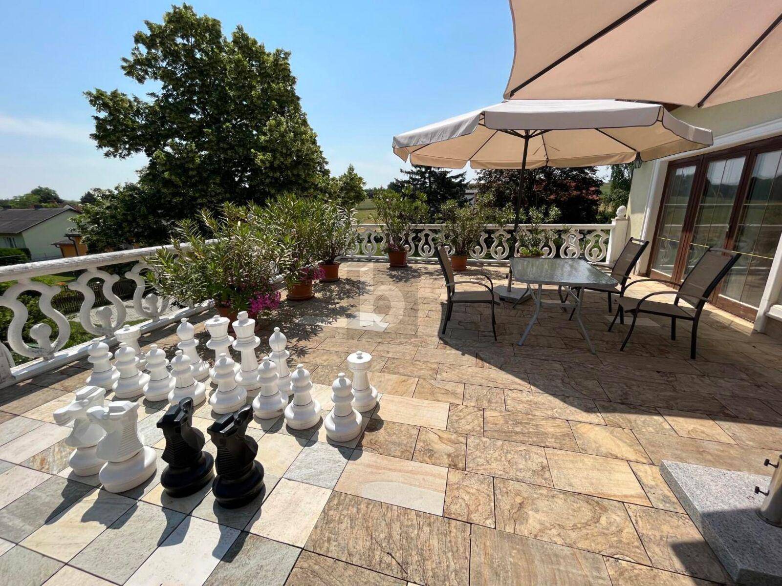 Geräumige Steinterrasse mit großem Schachspiel, Gartenmöbeln und dekorativem Geländer.
