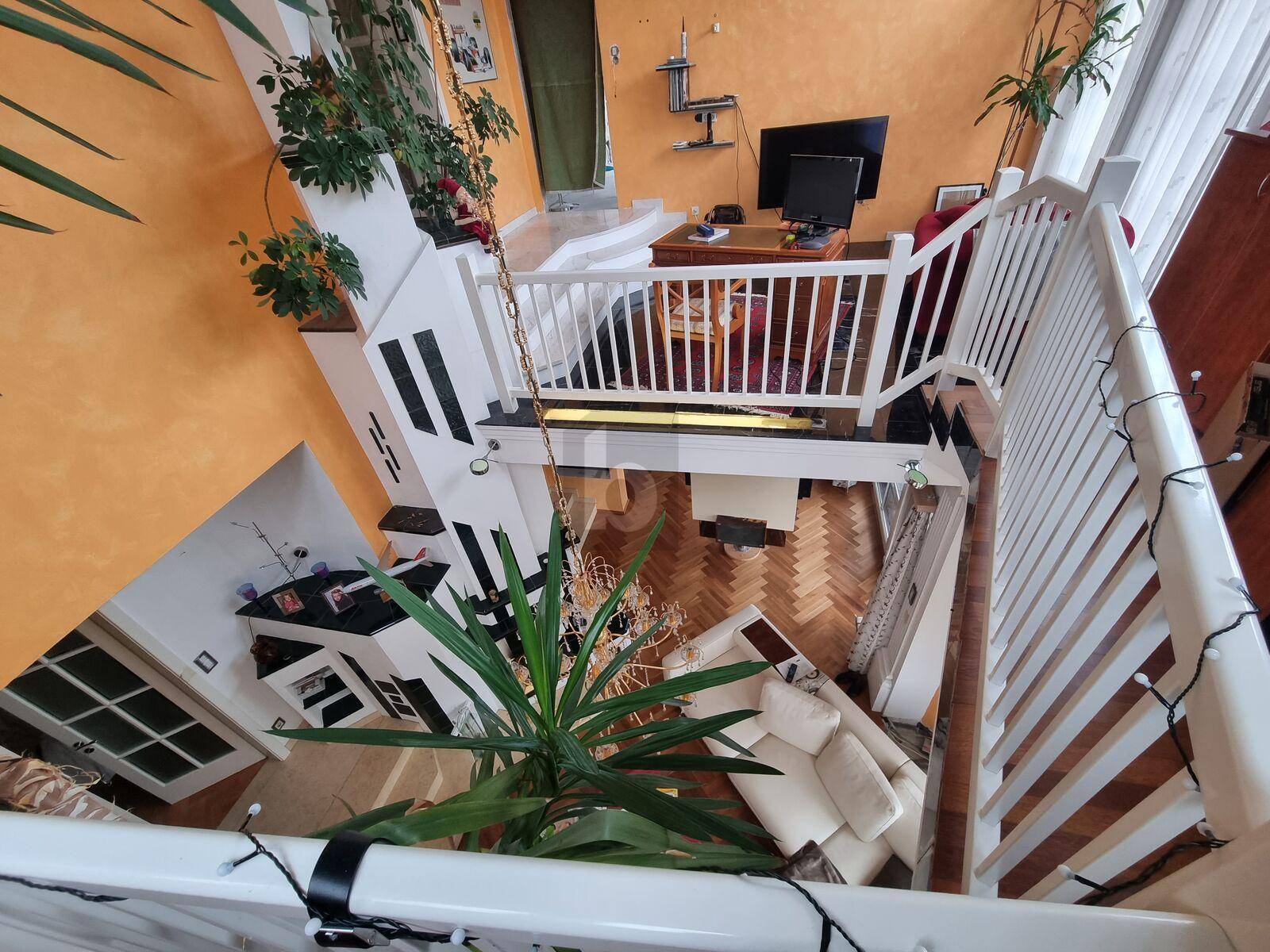 Blick von der Galerie in das offene Wohnzimmer mit hohen Decken und Holzparkett.