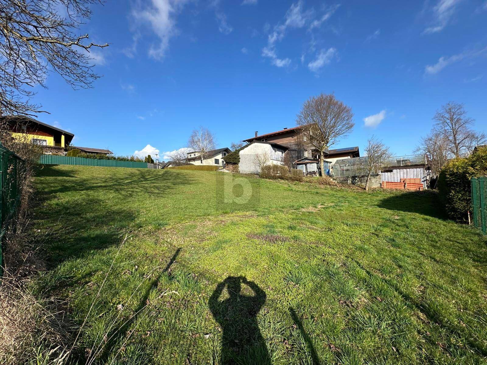 Sanft abfallende grüne Wiese mit mehreren Häusern im Hintergrund unter klarem blauem Himmel.