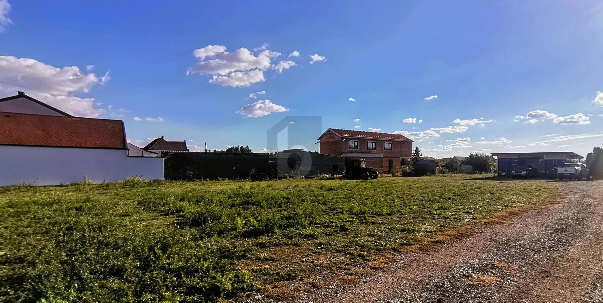 Weitläufiges unbebautes Grundstück mit Grasfläche und Häusern im Hintergrund unter blauem Himmel.