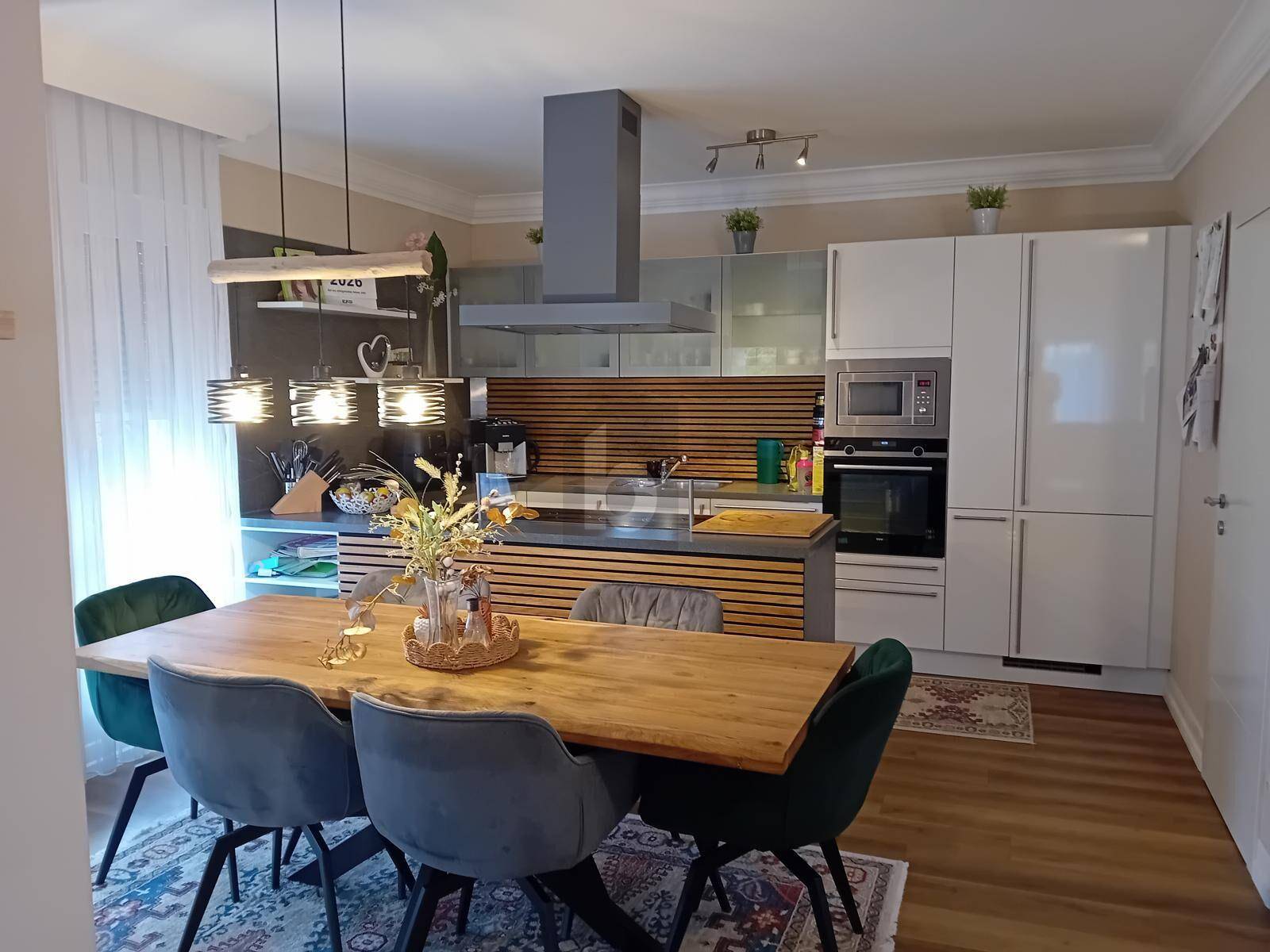 Moderne Küche mit Essbereich, hellen Schränken, Holzdetails und Dunstabzugshaube über der Kochinsel.