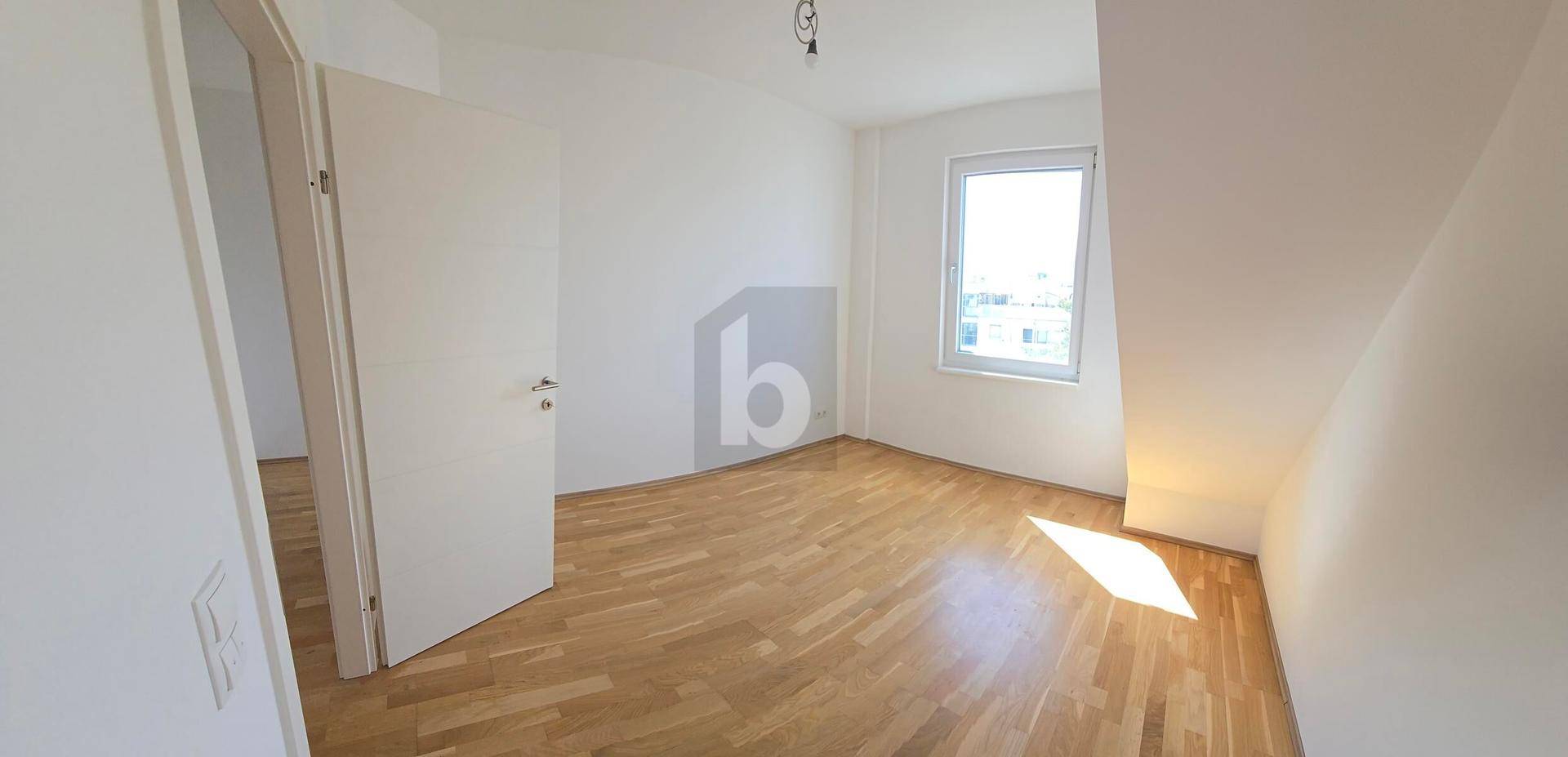 Geräumiges Dachgeschosszimmer mit Holzboden, einem Fenster und schrägen Wänden, ideal als Schlafzimmer.