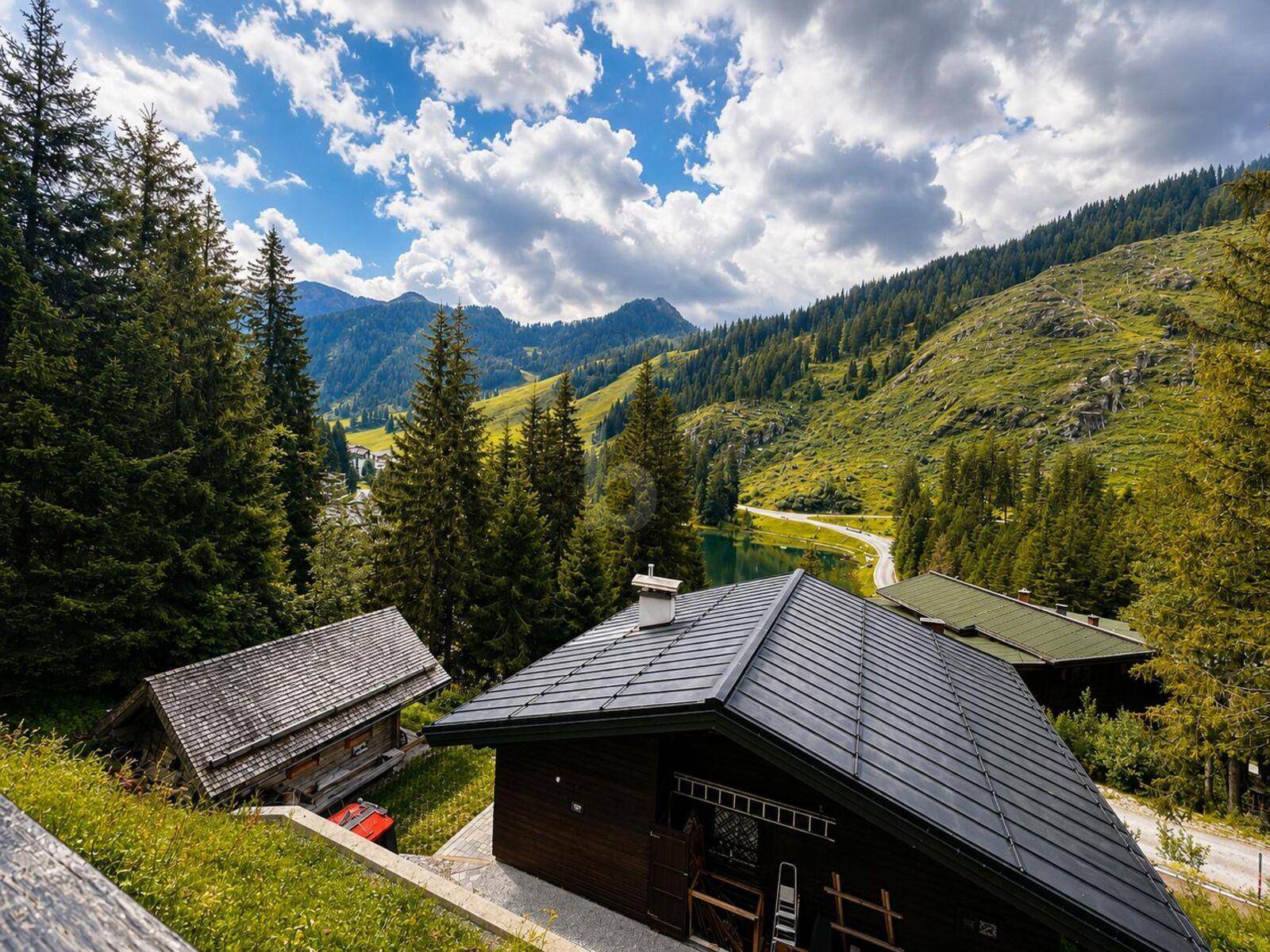 Panoramablick auf einen Bergsee und umliegende Häuser in einer grünen Alpenlandschaft.
