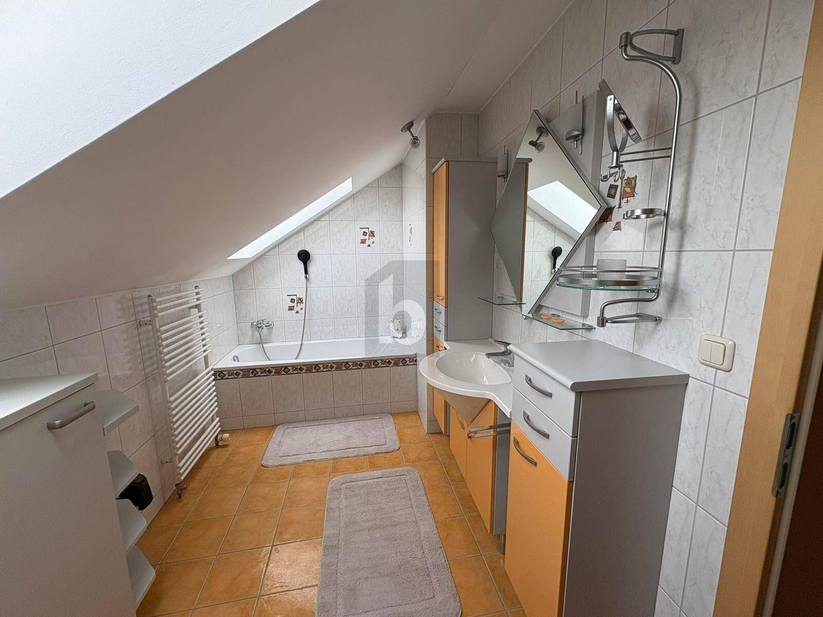 Helles Badezimmer im Dachgeschoss mit Badewanne, Dachfenster und Fliesenboden.