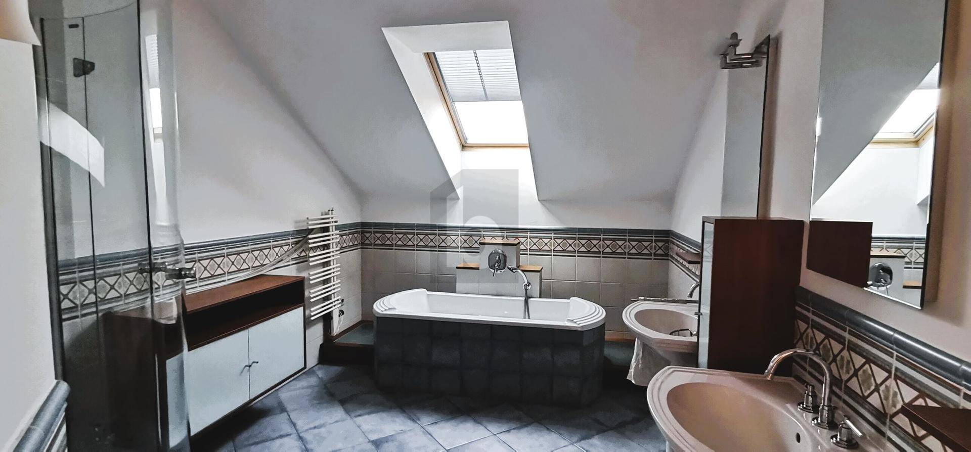 Badezimmer im Dachgeschoss mit Badewanne, Dusche, Doppelwaschbecken und Dachfenster.