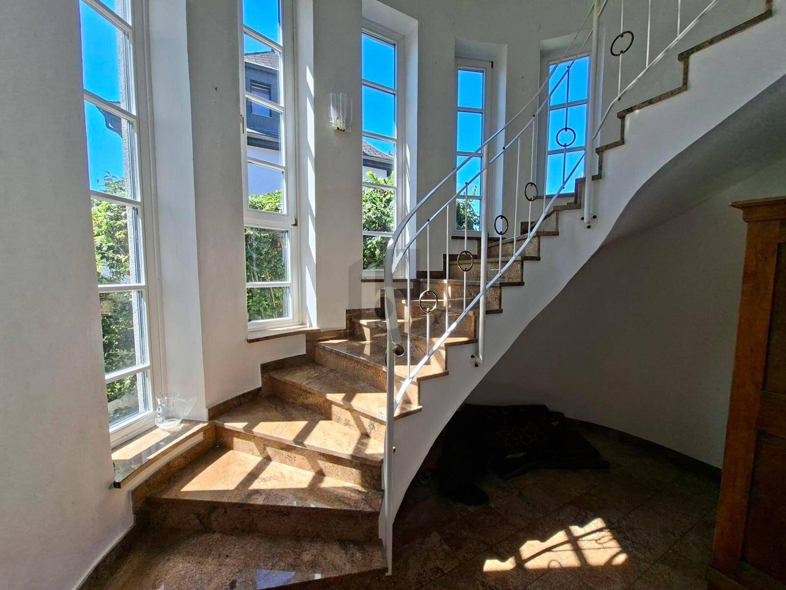 Elegante geschwungene Treppe mit Marmorstufen und hohen Fenstern für viel Tageslicht.