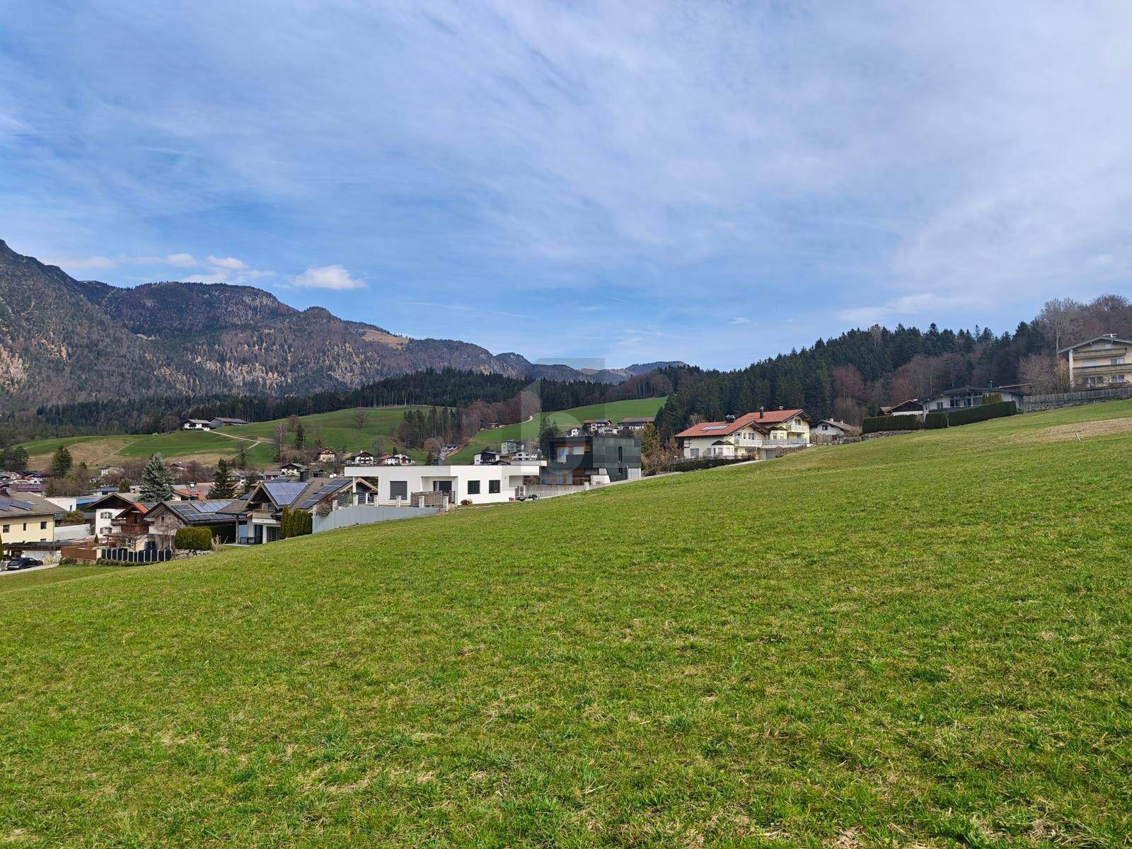 Weitläufige grüne Wiesen mit Blick auf eine Siedlung und die umliegende Berglandschaft.