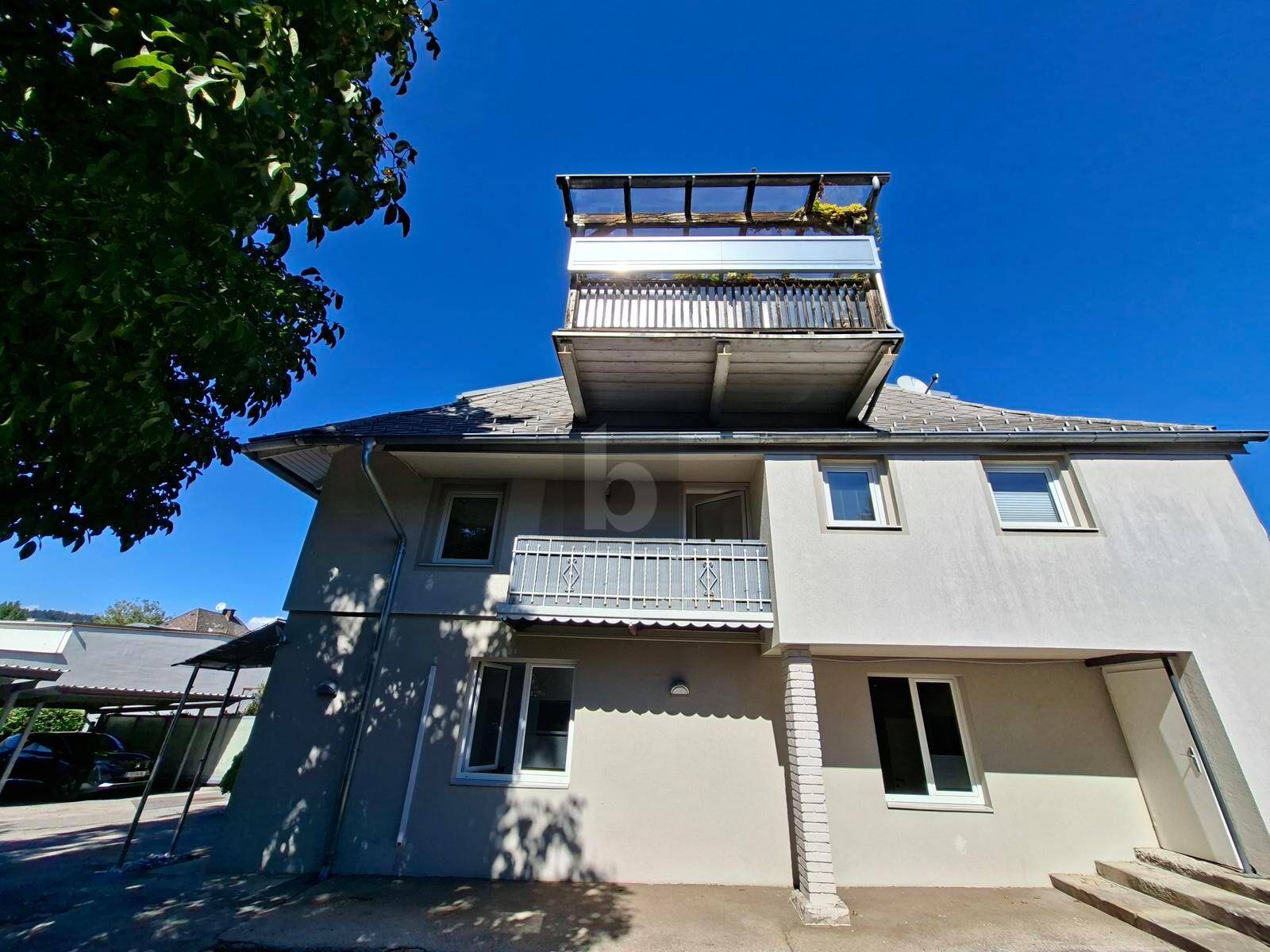 Rückansicht des Gebäudes mit Balkon, Dachterrasse und einem überdachten Stellplatz.