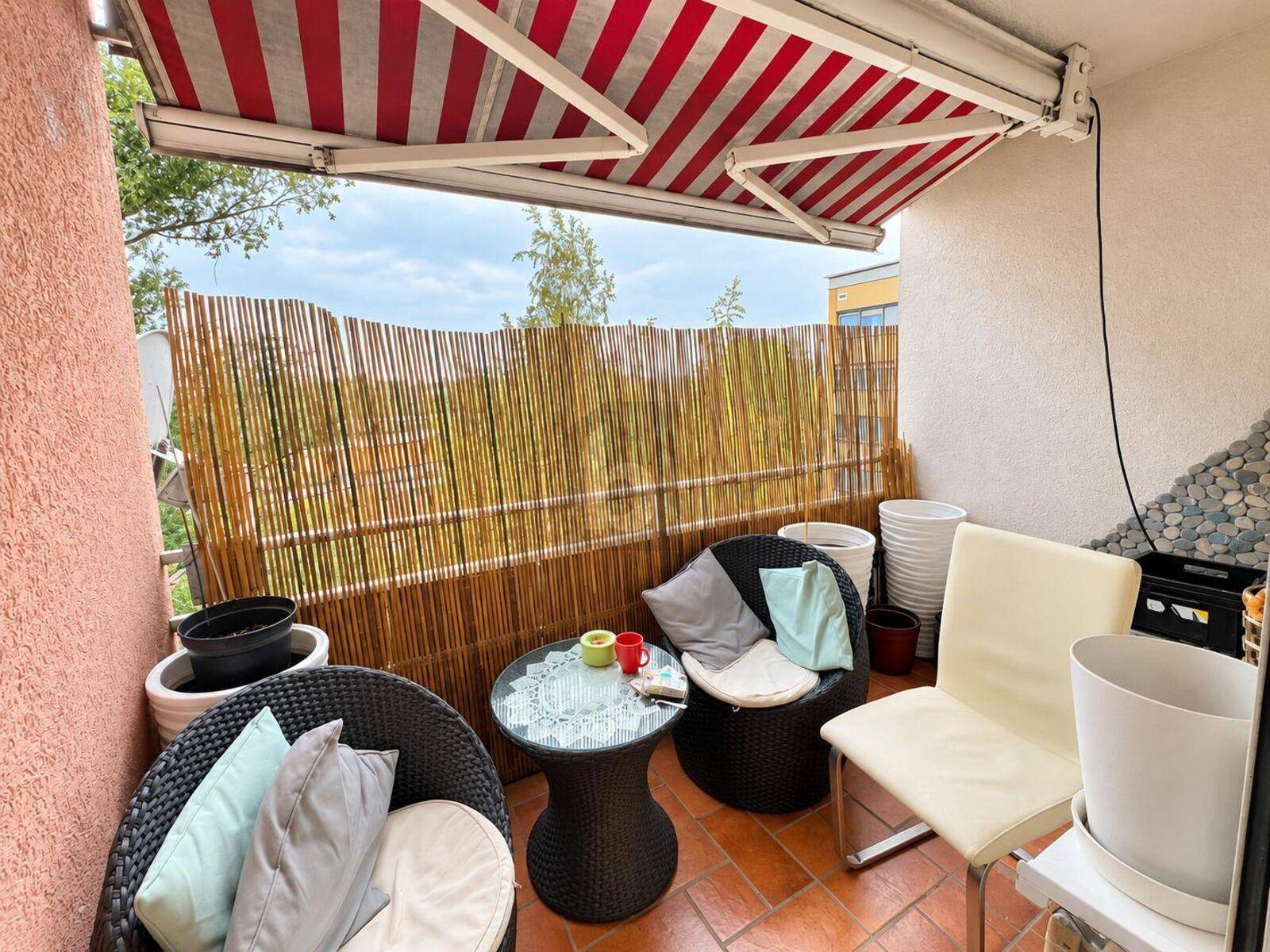 Kleiner, gemütlicher Balkon mit Markise, Sitzgelegenheiten und Bambus-Sichtschutz.